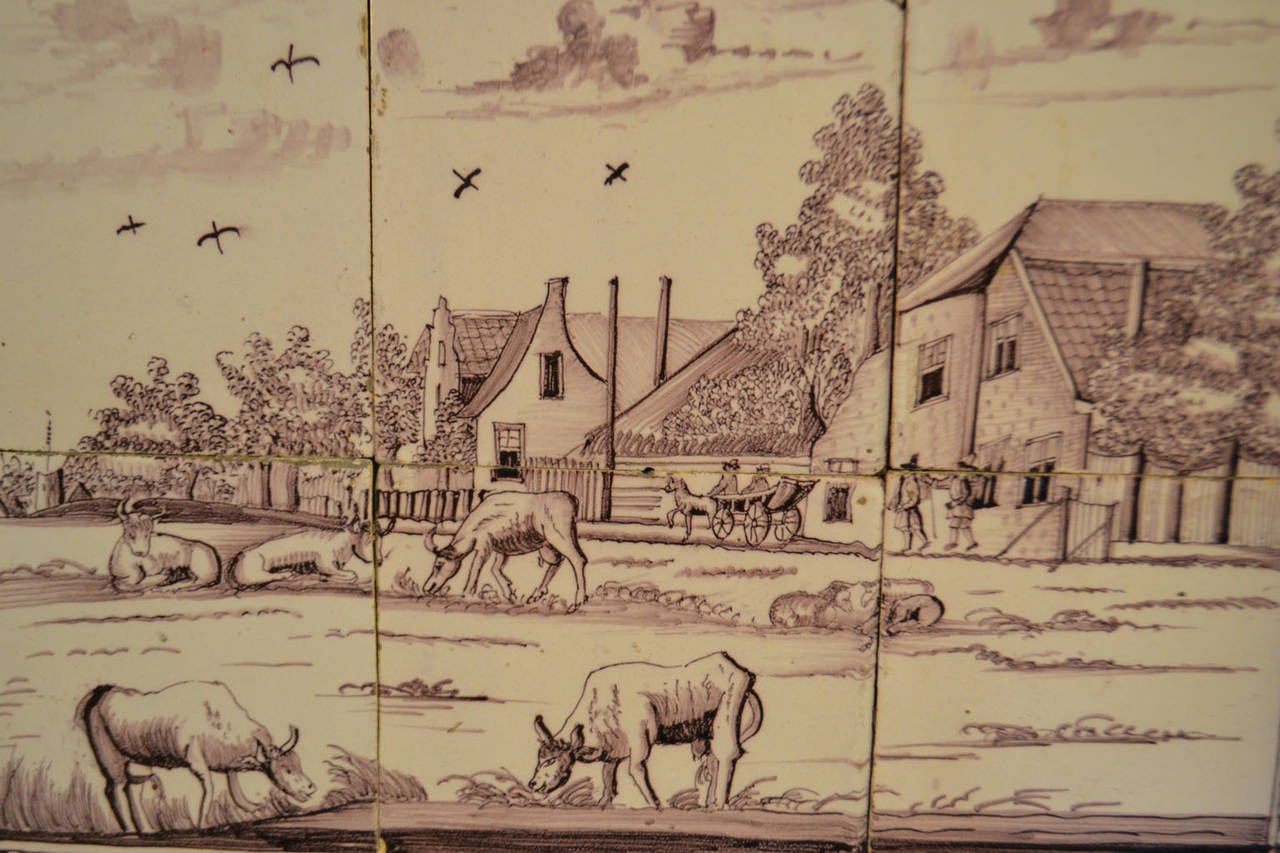18th century delft tile wall picture of landscape: cows grazing in the forefront, people, and horse and carriage traveling through a village with birds flying overhead in a cloud swept sky.