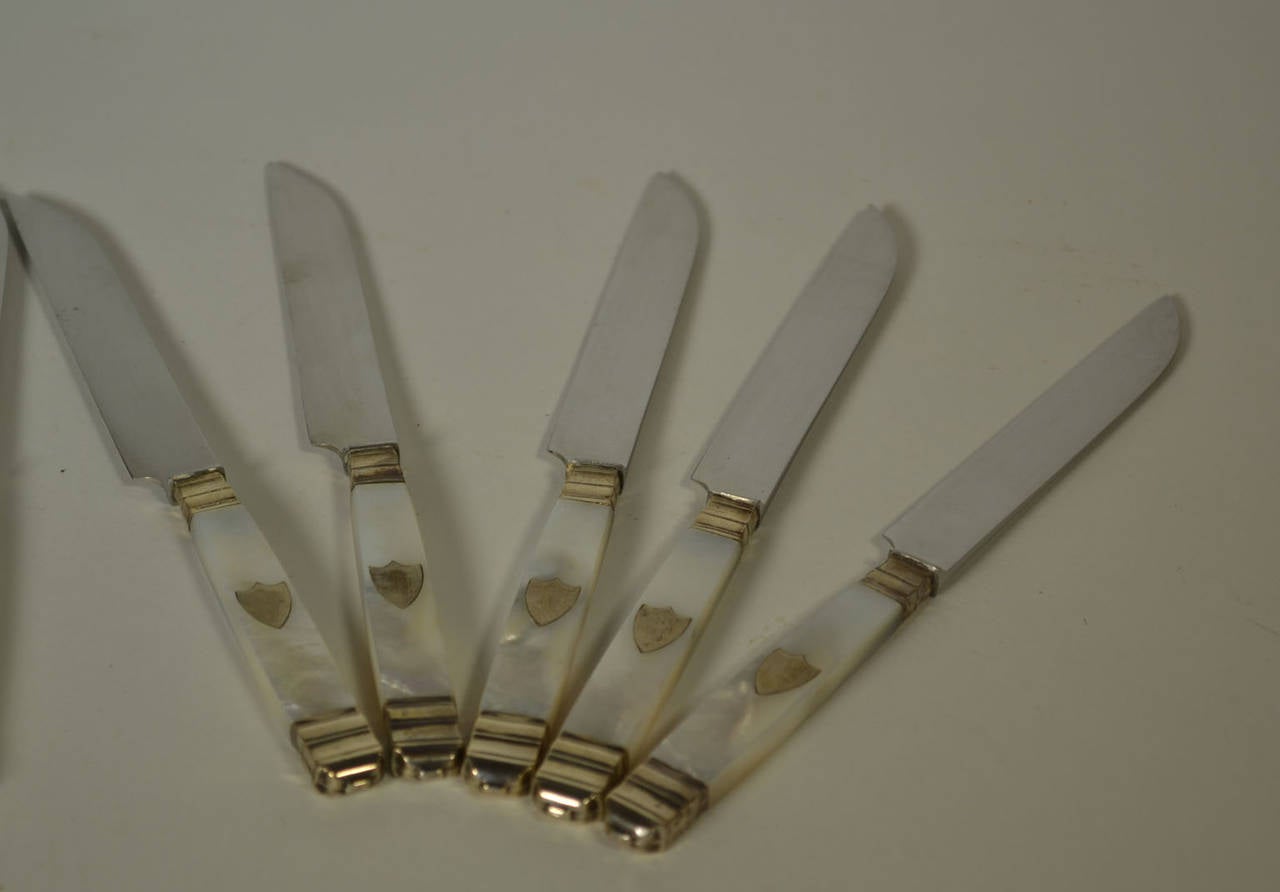 Set of 12 sterling and mother-of-pearl handled dessert knives with shield emblem and stainless steel blades (Inoxydable), circa 1890.
