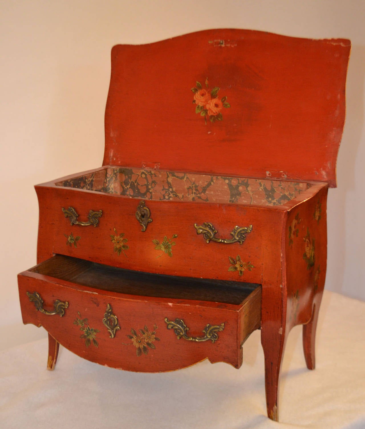 An exceptional small painted commode (apprentice piece) in red, gold, and floral design signed Germaine et Roger Antiquites, Paris. This piece has one drawer and a larger faux drawer that lifts from the top, and inside there is faux marble paper