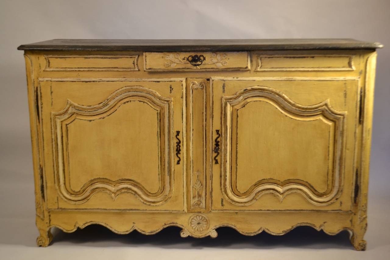 Wonderful Louis XV buffet, painted yellow, with conforming frieze, and a simple yet elegant carved molding in bow shaped transoms. The central rosette rests between two scrolls on a bow shaped apron raised on scroll feet. There is some finely carved