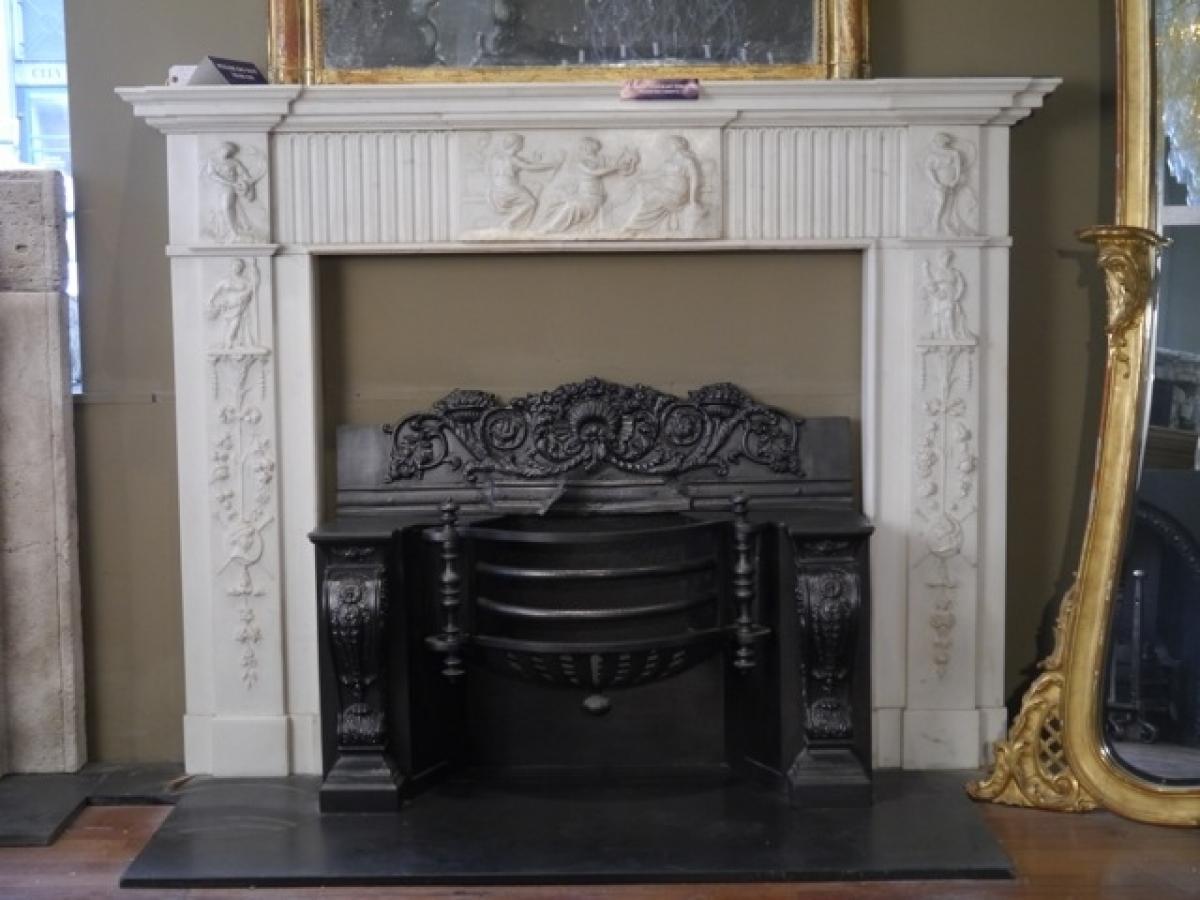 An original statuary white Georgian 18th century marble fireplace in the manner of Robert Adam, with a centre plaque and corner blocks depicting Greek muses and fluting either side of centre plaque and heavily decorated jambs.