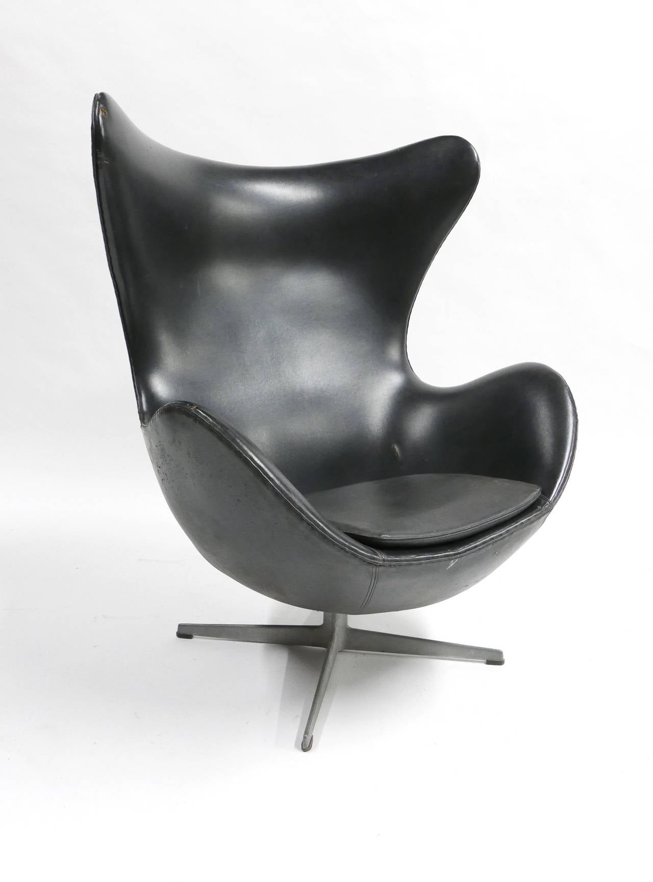 A black Jacobsen swiveling egg chair with aluminum base and rubber footpads. Production markings on base, manufactured by Fritz Hansen made in Denmark. This chair is a great candidate for re-upholstery although useable as is the original vinyl