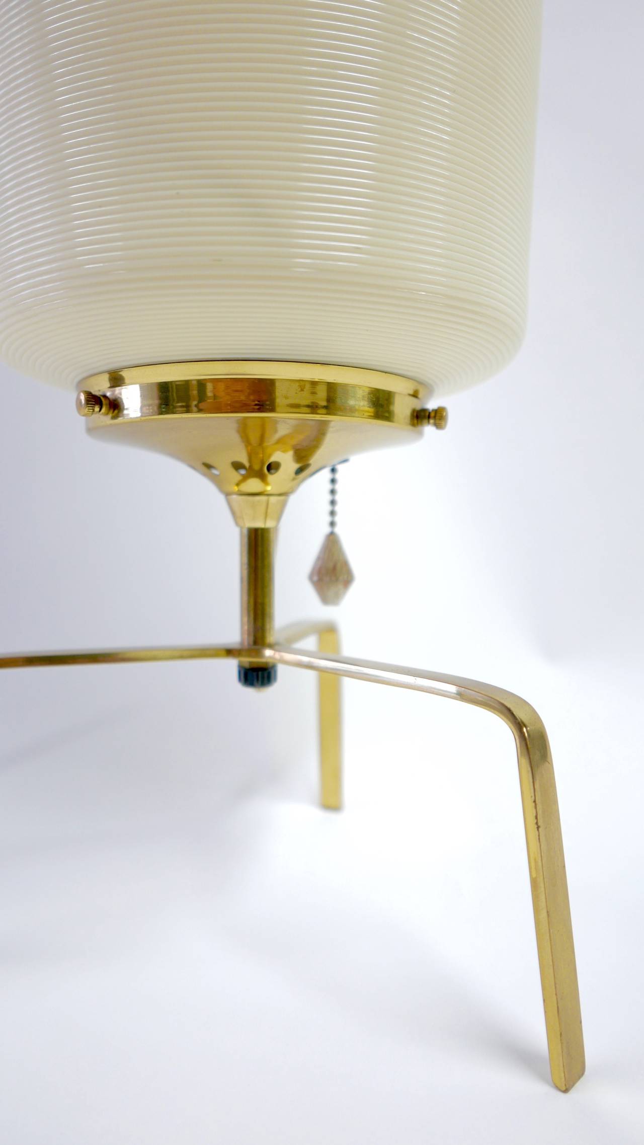 A cylinder shaped table lamp with a brass tripod base.     The Rotoflex plastic shade has contrasting hues of crème and tan.  Produced by the Heifetz Lighting Company.