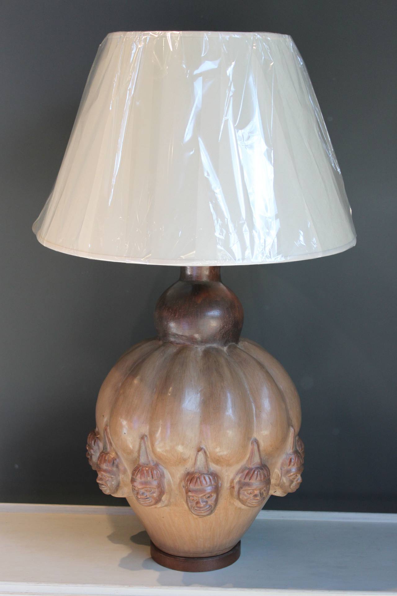 Monumental pottery gourd-shaped lamp with figured heads resting on a wood base. This lamp has been rewired and includes a new shade. This exceptionally large lamp has a wonderful warm patina. 

The lamp itself is 16.5