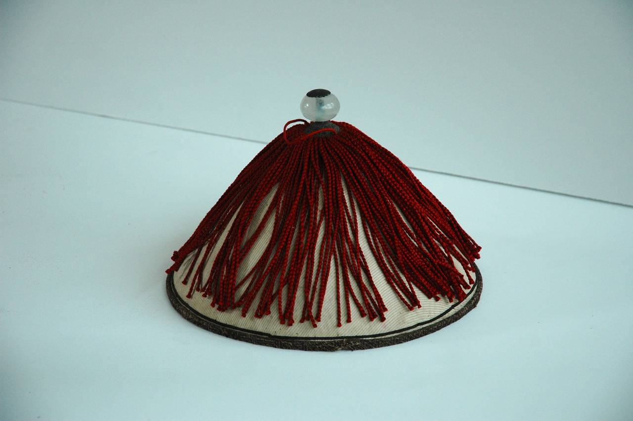 A Chinese mandarin summer hat with red silk tassel trim and glass finial top. Includes antique Chinese leather hat box.