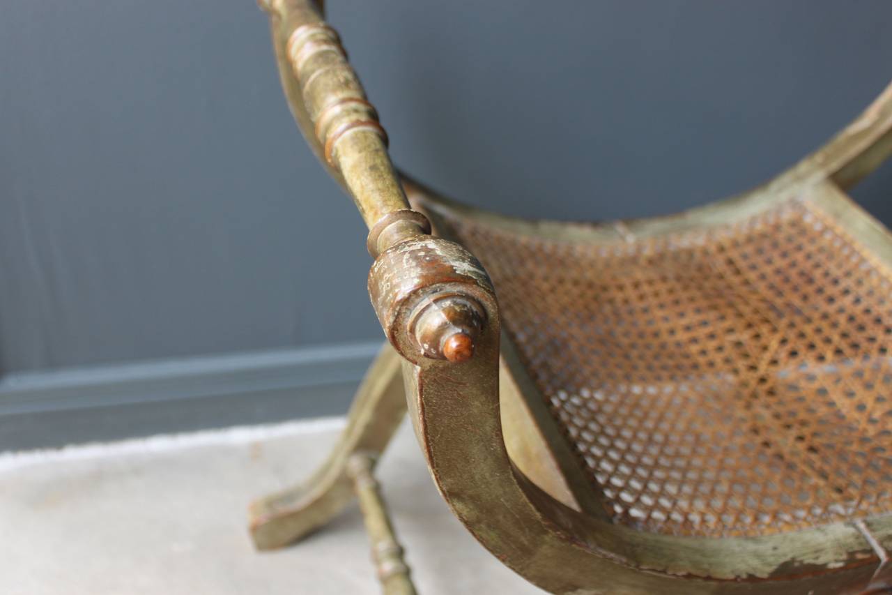This lovely 19th century French curule tabouret or stool has a caned seat and original traces of green/gray paint and gilding. The caning has some damage as does one of the round carved details. The piece has a lovely worn patina.