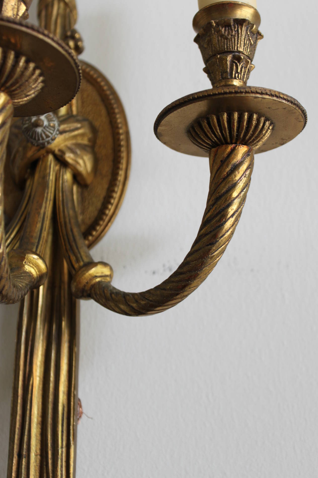 Vintage pair of brass neoclassic French wall sconces with three arms. Each of Classic form with looped tassel detail and crossbanding.