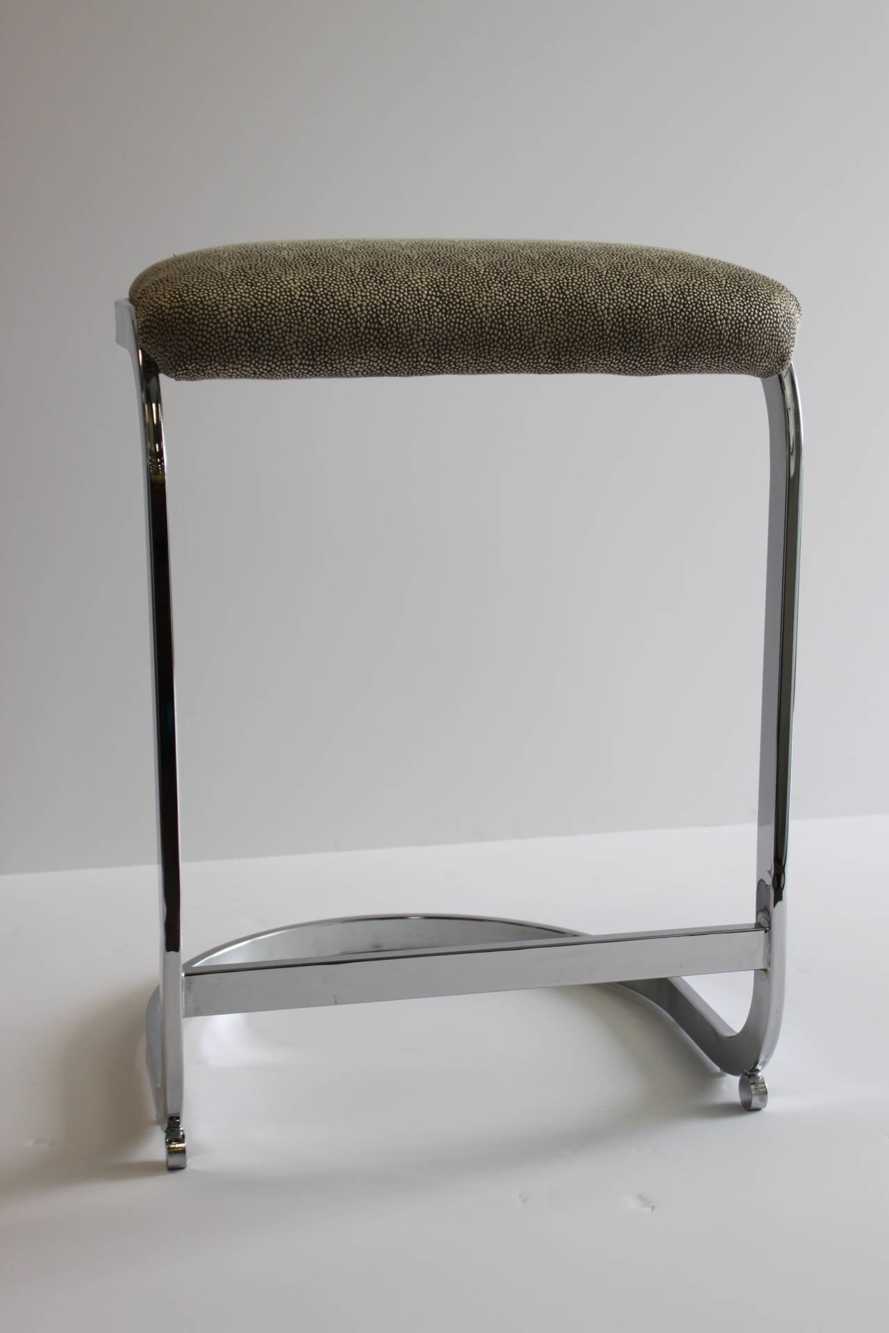 Pair of counter height chrome stools in the style of Milo Baughman. These stools have been newly upholstered in a stylized faux shagreen fabric, circa 1970s.

Measures: 23 1/2