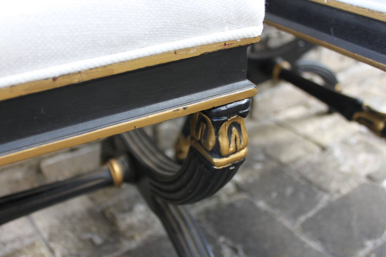 Pair of Regency-style newly-upholstered stools or ottoman benches in a black and gilt finish.
