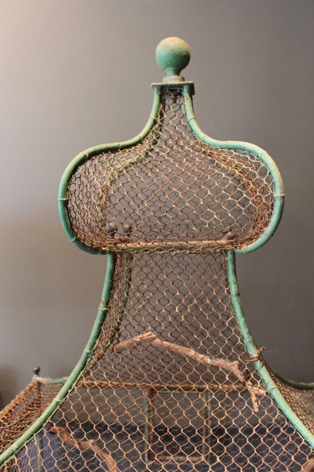 Wonderful and monumental 19th century French green painted bird cage. This bird cage has a fantastic worn painted finish and various wooden twigs wired to interior. Legs are on casters and top has a pagoda shape detail with ball finials at the top
