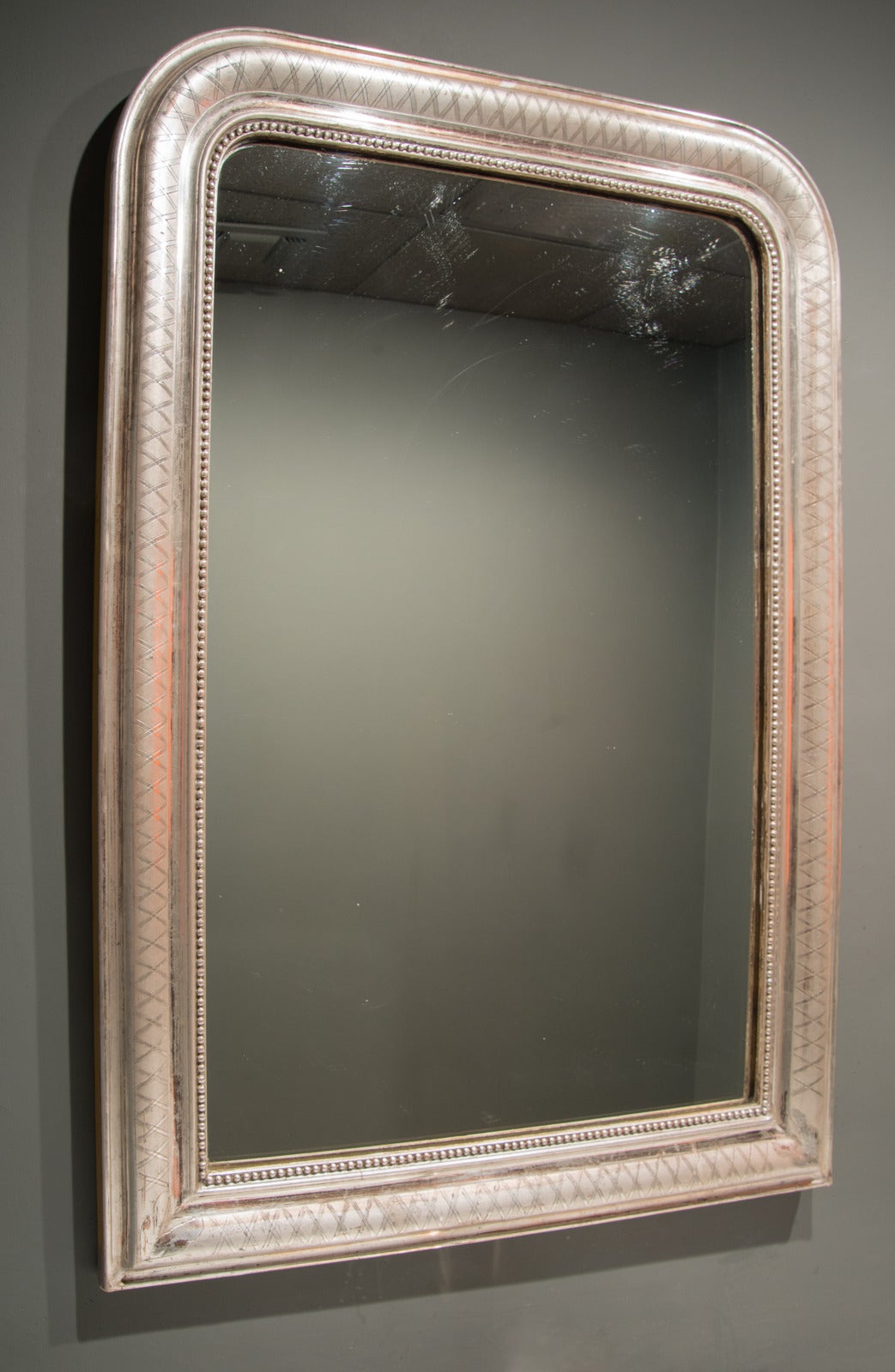 This Louis Philippe mirror is from France in the 19th century. The finish is silver gilt with a bead detail along the inner edge as well as a cross-hatch pattern along the front of the frame. The overall appearance of this mirror is quite lovely,