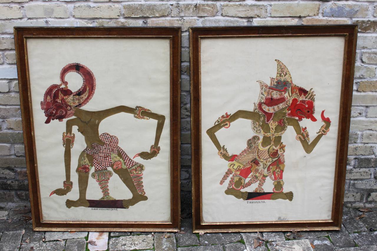 Pair of paintings on paper depicting wayang kulit also known as shadow puppets. These Indonesian folk paintings are on paper under glass with lovely aged burled wood frames. The paintings are likely early 20th century and frames are most certainly
