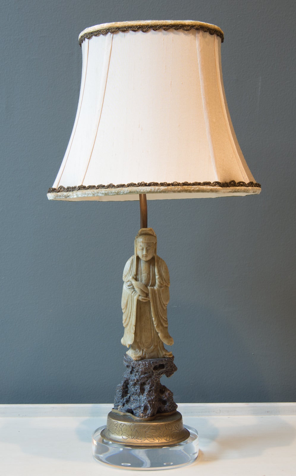 This lamp features a Chinese green hard stone female standing figure on the original bronze and brass base mounted to a new Lucite base. Also included is a custom ecru silk shade with pale green trim.
