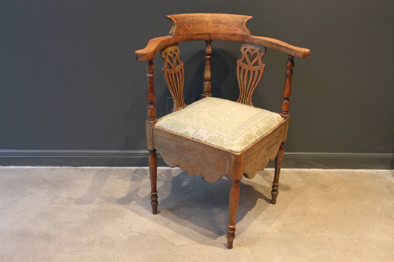 Corner chair with a delicate pierced back splat containing a heart. The chair retains remnants of the original painted finish. The chair has turned legs and rails and a deep carved apron. The seat has been newly upholstered in a green and cream