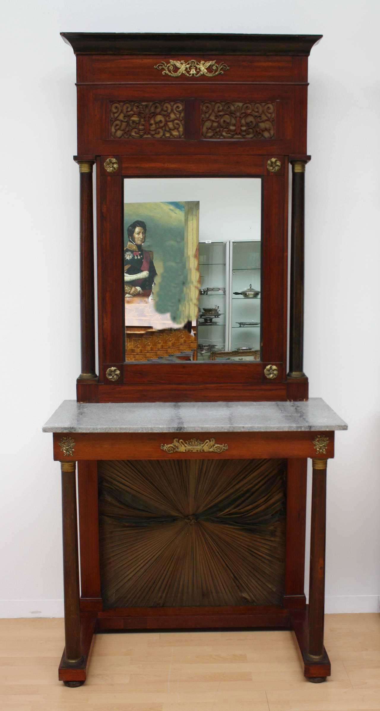 Gorgeous pair of Austrian Empire consoles with mirrors. Mahogany and nutwood consoles with grey marble tops, back with sun shaped shirred fabric. Columns and front with finely modelled bronze Mounts. Above mirrors openworked carved, backed with