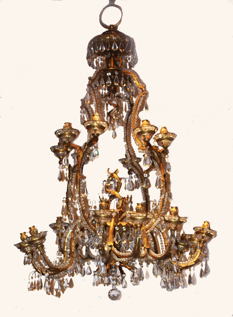 This beautiful ornate crystal and gilt iron twenty-light chandelier is comprised of two tiers of candle fittings with the top tier having eight candleholders and the bottom tier having 12 candleholders. The chandelier is decorated with faceted