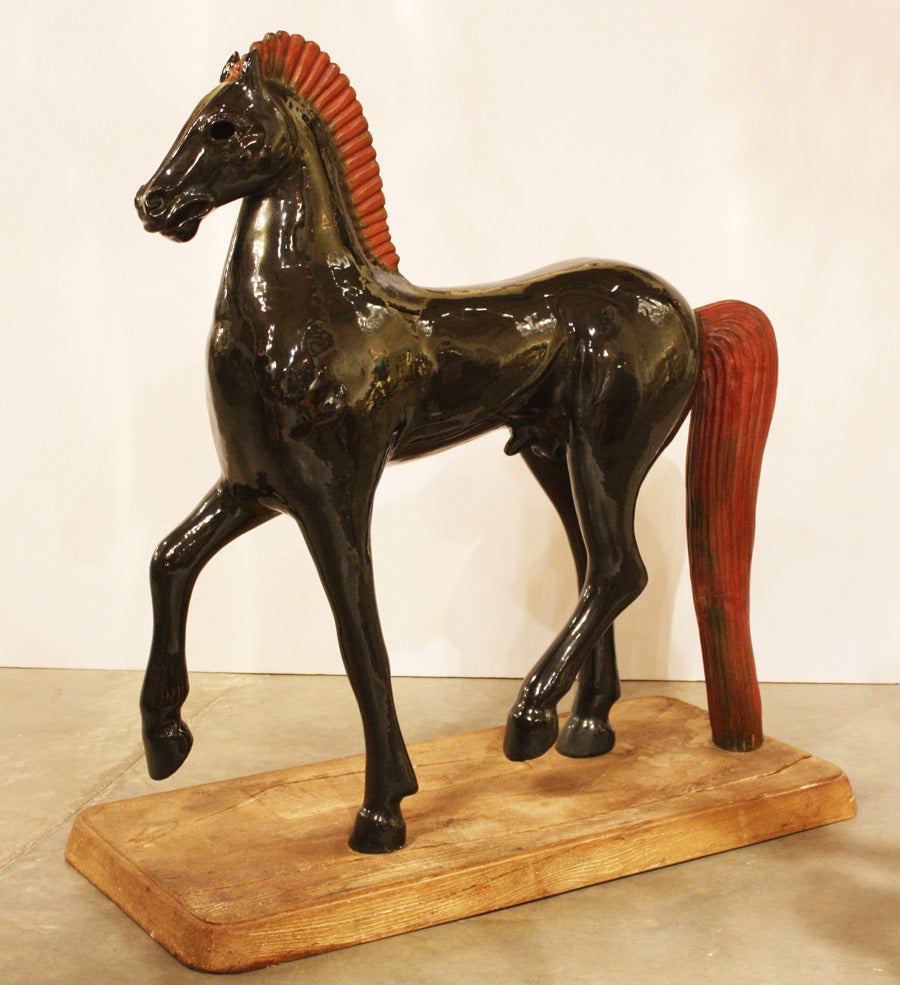 This large-scale red and black glazed ceramic horse figure is heavily influenced by Etruscan sculptural styles from antiquity and is mounted on a weathered wood base.