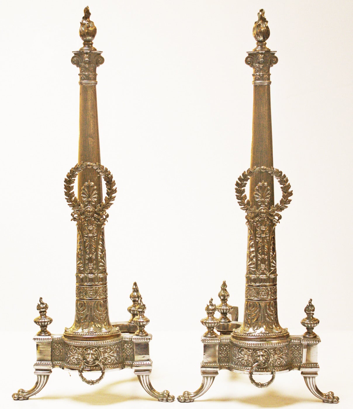 Regency inspired silvered metal andirons with flames, finials, paw feet and laurel wreaths.