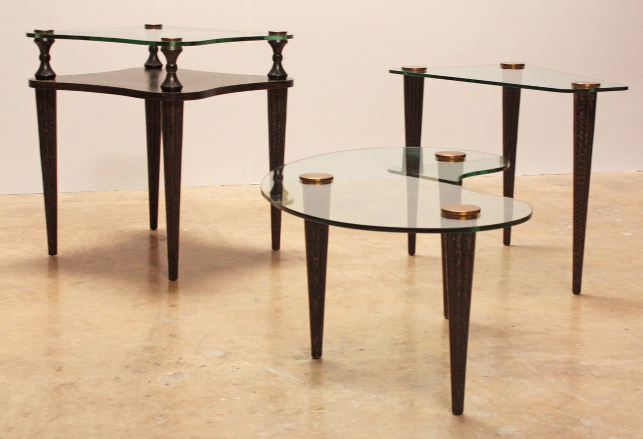 Set of three circa 1950 ebonized and limed oak biomorphic tables with bronze mounted glass surfaces in the manner of Gilbert Rohde. Square table has additional shelf. Tables also sold separately. Listing size reflects the measurements for the square