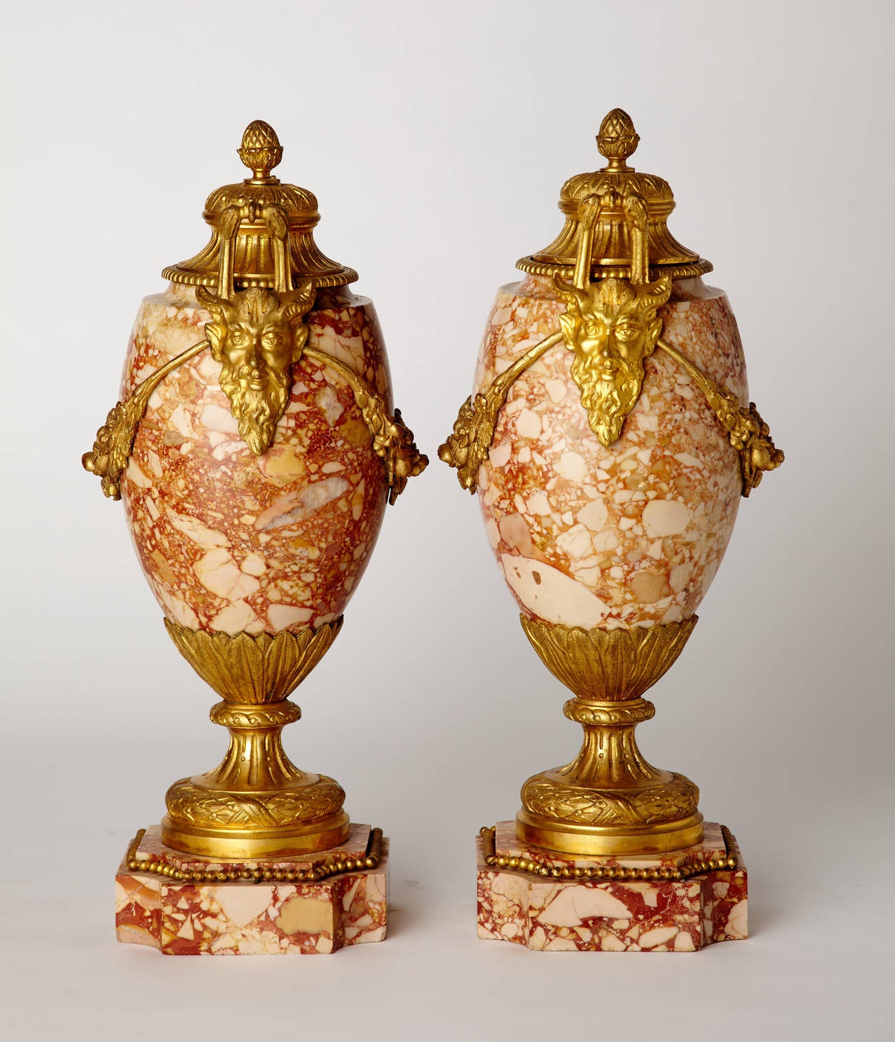Zwei französische Marmorvasen im Stil Ludwigs XVI. um 1900 mit fein gearbeiteten, vergoldeten Bronzebeschlägen. Die vergoldeten Bronzeschwänze enden in Griffen, die durch Satyrmasken verankert sind. Abnehmbare Deckel aus vergoldeter Bronze.