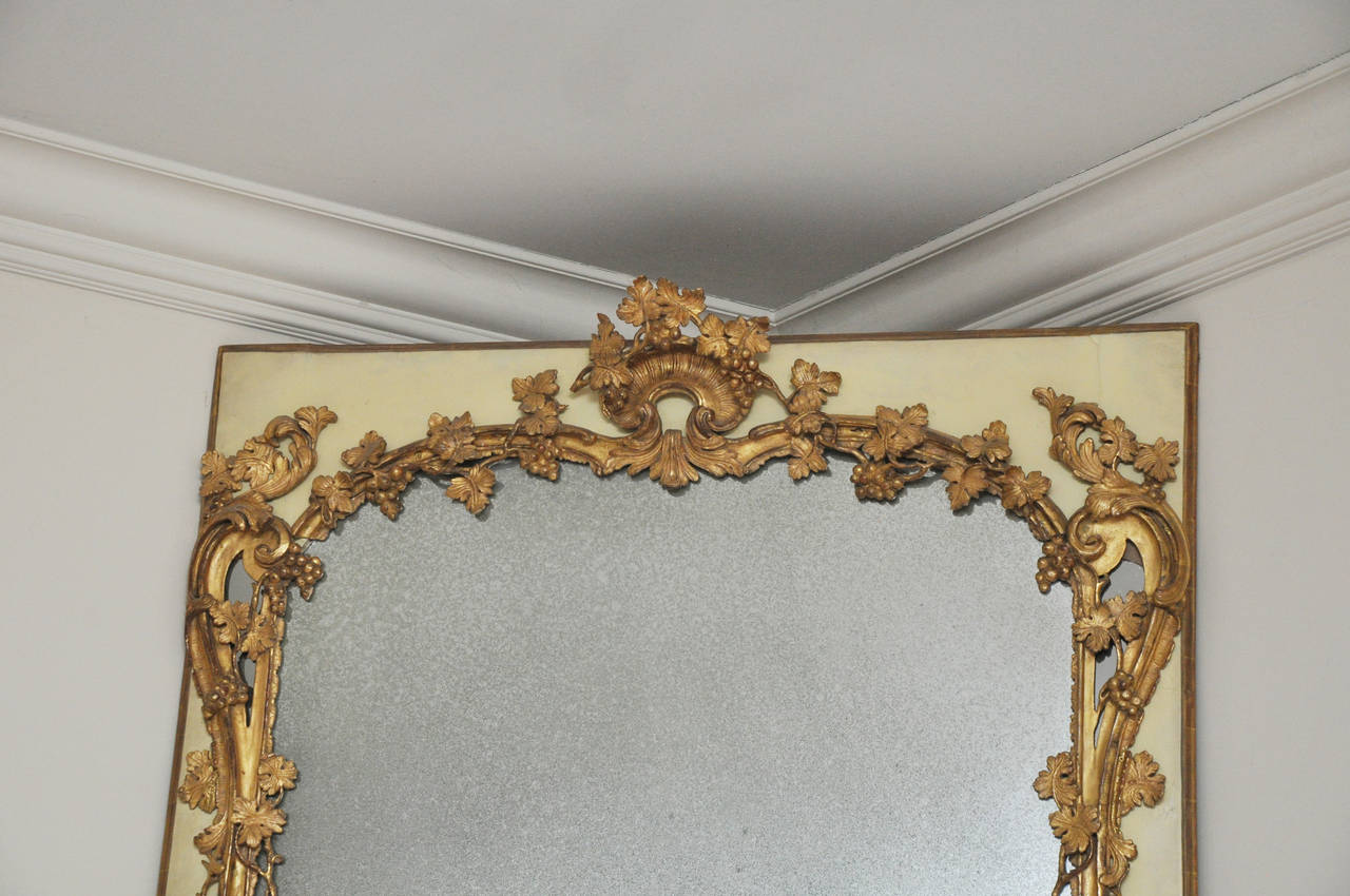 Magnificent hand-carved 18th century French Trumeau mirror. Original painted surround in crème color.

Beautiful giltwood mirror found in a large chateau from the Provence region of France. Elaborate grape/grapevine carvings traverse both top and
