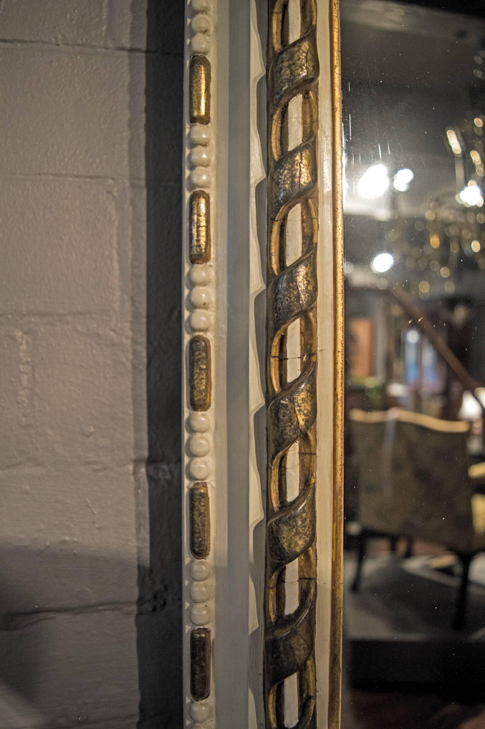 A very smart overmantel mirror with its stunning original sparkling glass plate. The parcel-gilt and painted frame of simulated rope twist and beaded edge design with leaf scrolls on ebonised feet.