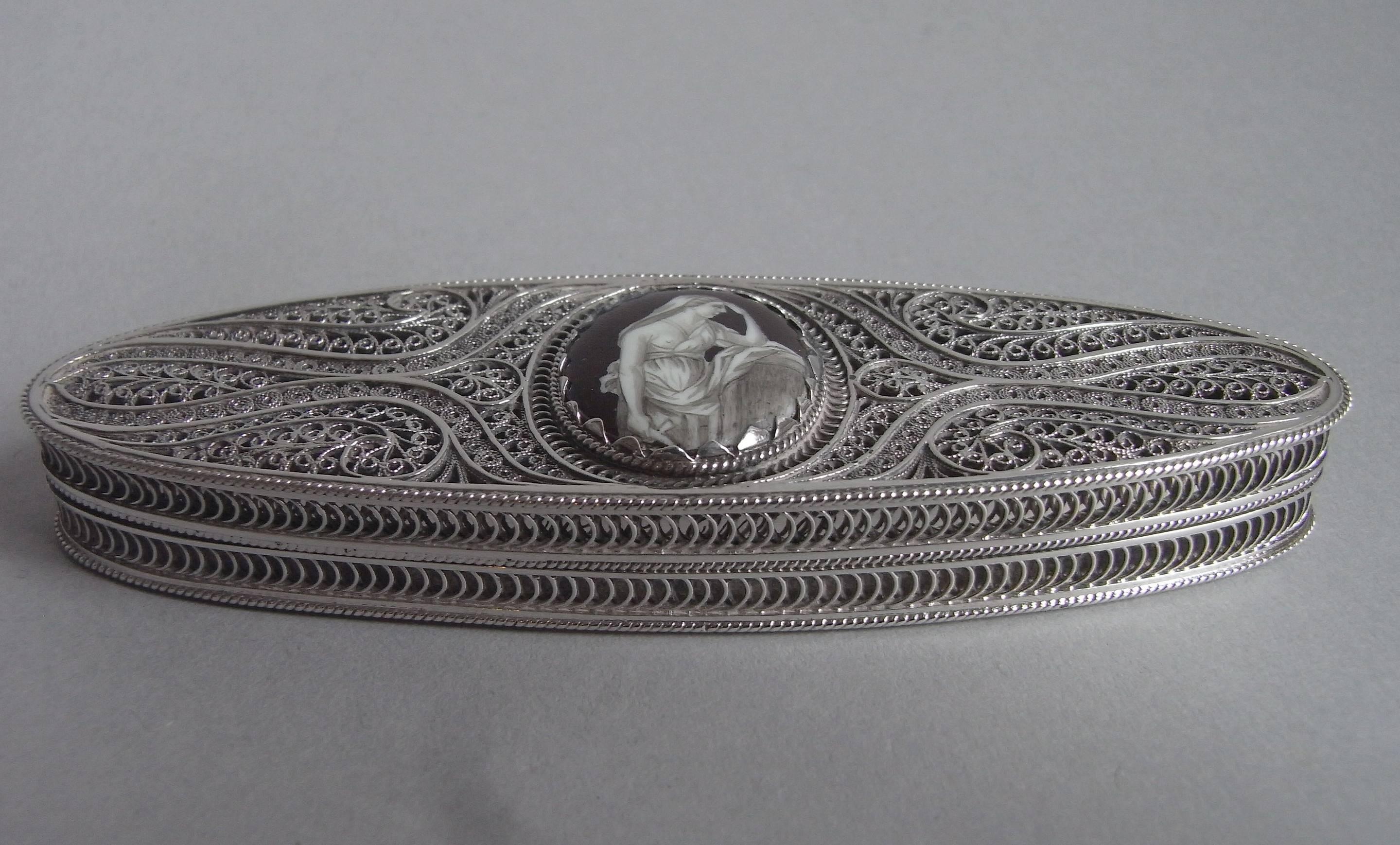 The Toothpick case is elliptical in form and is made entirely of filigree work. The cover and base display unusual scroll work designs and the cover also displays a beautiful domed oval enamel of a Classical female figure in flowing robes. The