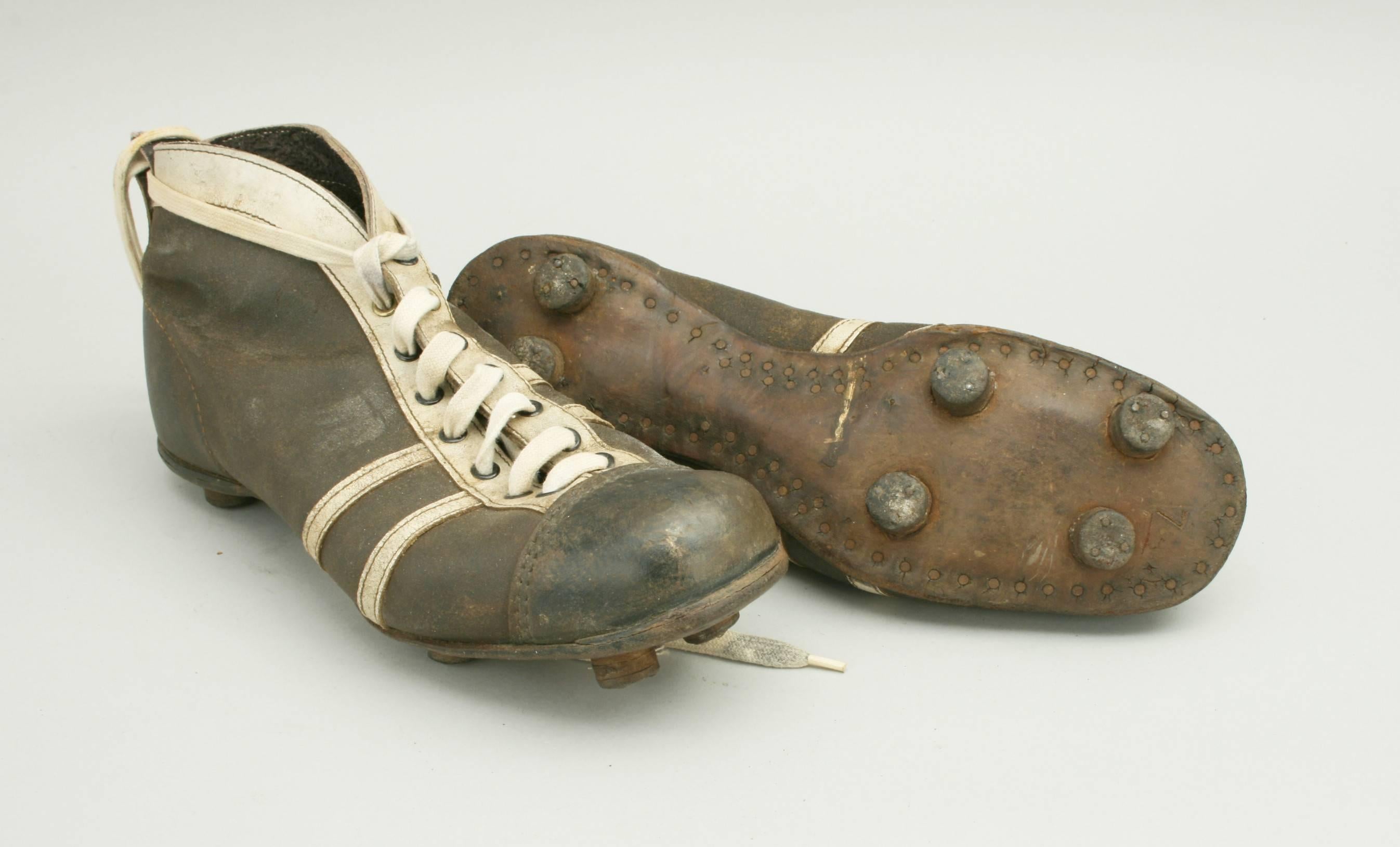 A pair of used black and white leather football boots. The toe area on the boots is made of hardened leather, as it was the normal play to toe-kick the football rather than use the instep as in today's game. The sole of the boots are fitted with 6
