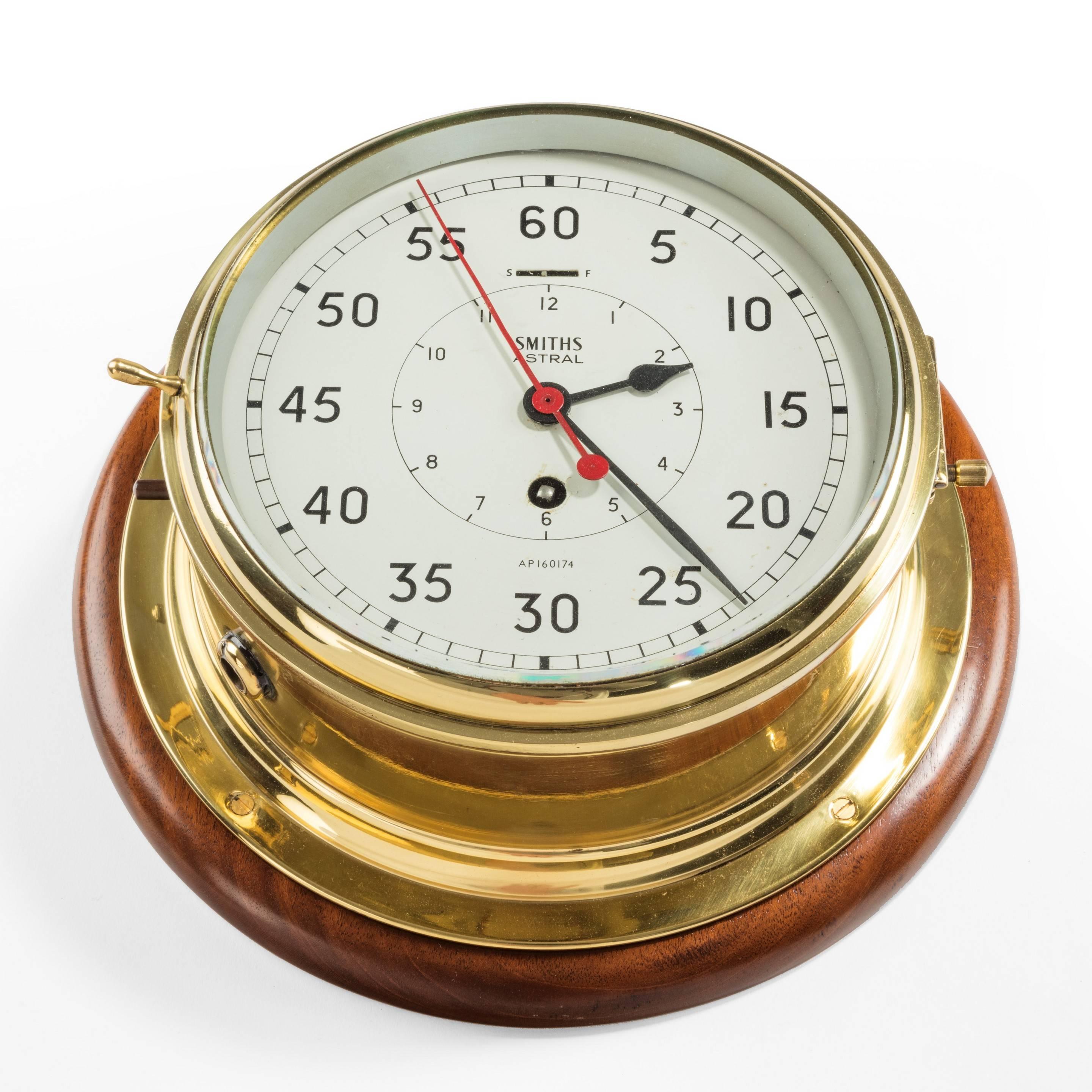 An 8 inch Smiths astral bulkhead clock, with a stop watch, on a mahogany backboard.