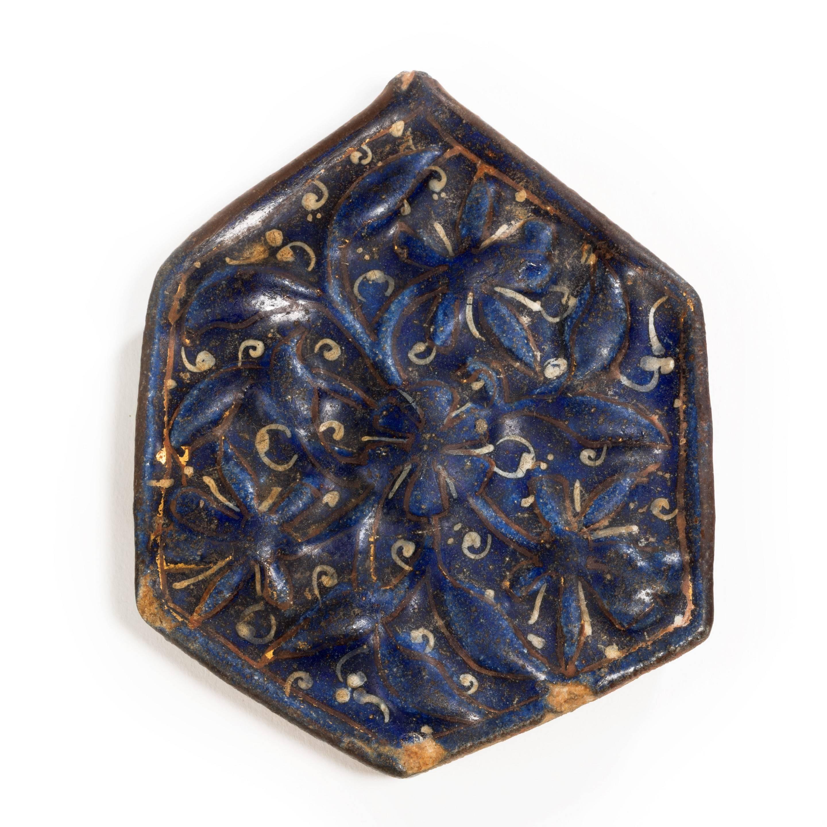 An Ilkhanid ladjvardina six-sided tile painted in underglaze blue with white scrolls and gilt highlights. Kashan (Iran), late 13th century.