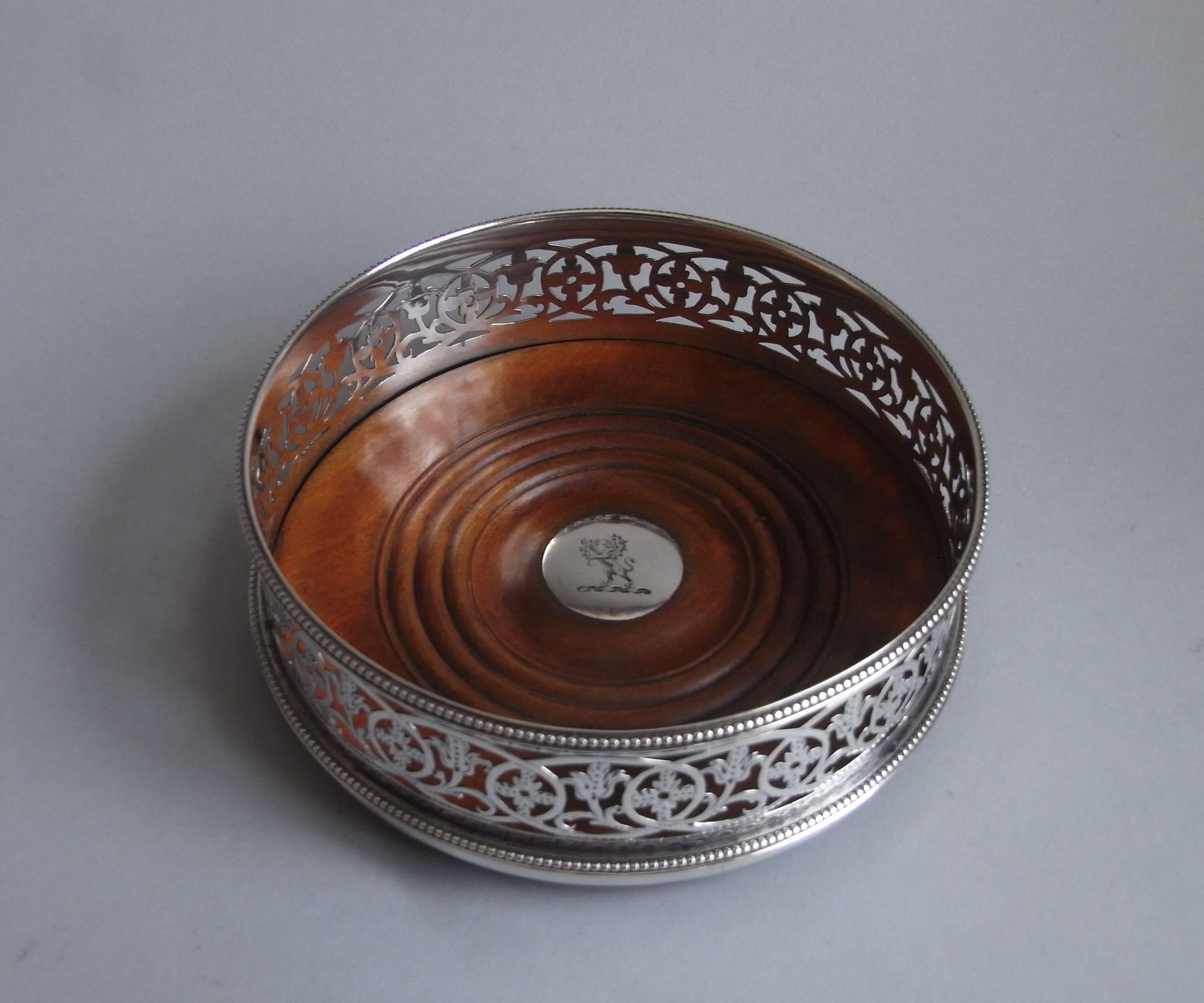 The wine coasters are circular in form and display deep sides decorated with a beaded band on the base and the rim. The sides are beautifully pierced and engraved with trailing floral sprigs and flower heads in ovals. The sides also display both