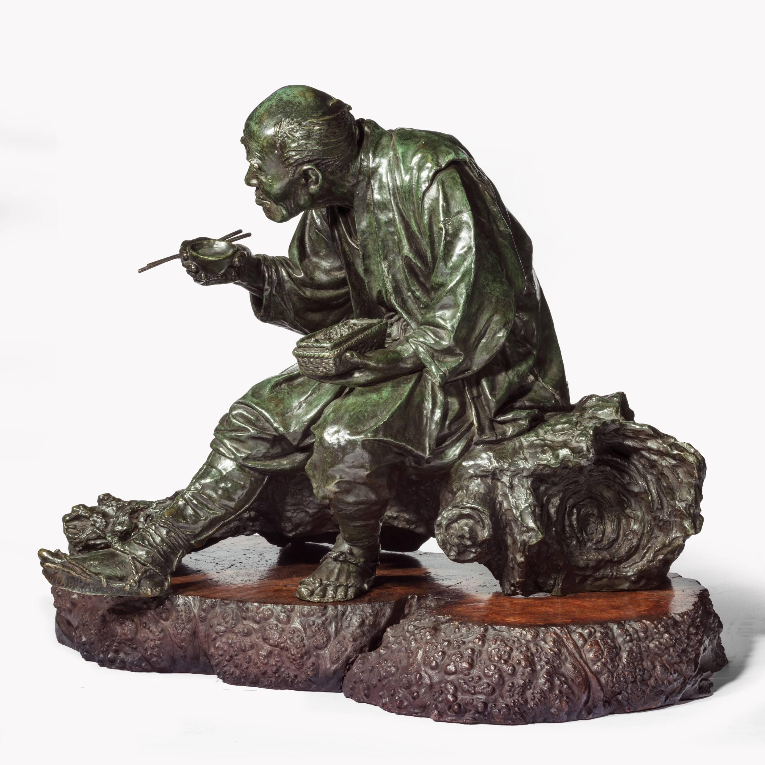A superb and large Tokyo school bronze of a peasant by Udagawa Kazuo,
He is shown sitting on a fallen tree branch eating his meal, holding a pair of chop sticks and a cup in his right hand and a woven basket of food in his left, with marvellous