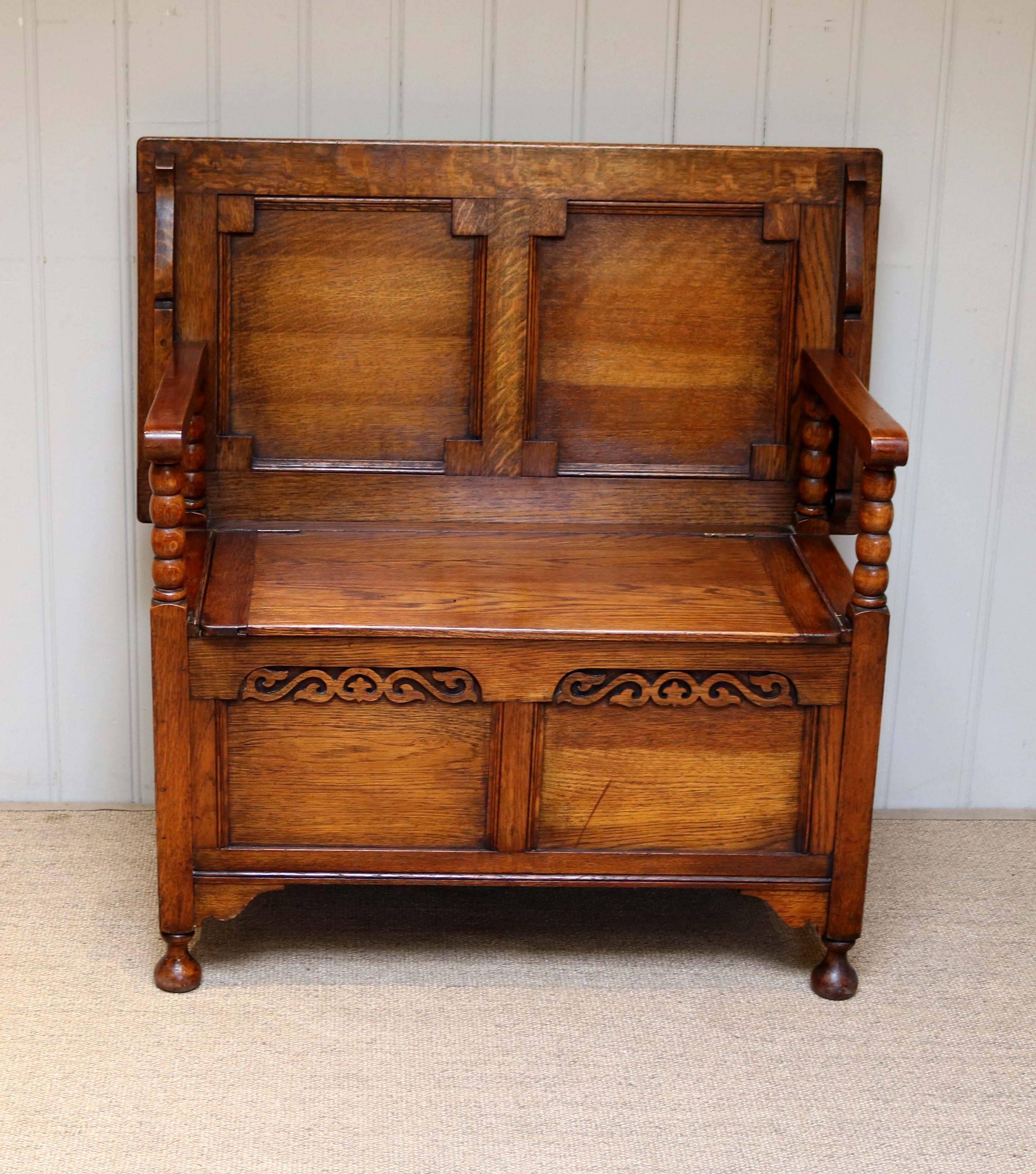 Golden oak monks bench having a panelled front and back with carved detail to the front edge with a lift up seat for storage and a top that folds to become a table having bobbin turned supports. Measure: The height when folded is 72cm.