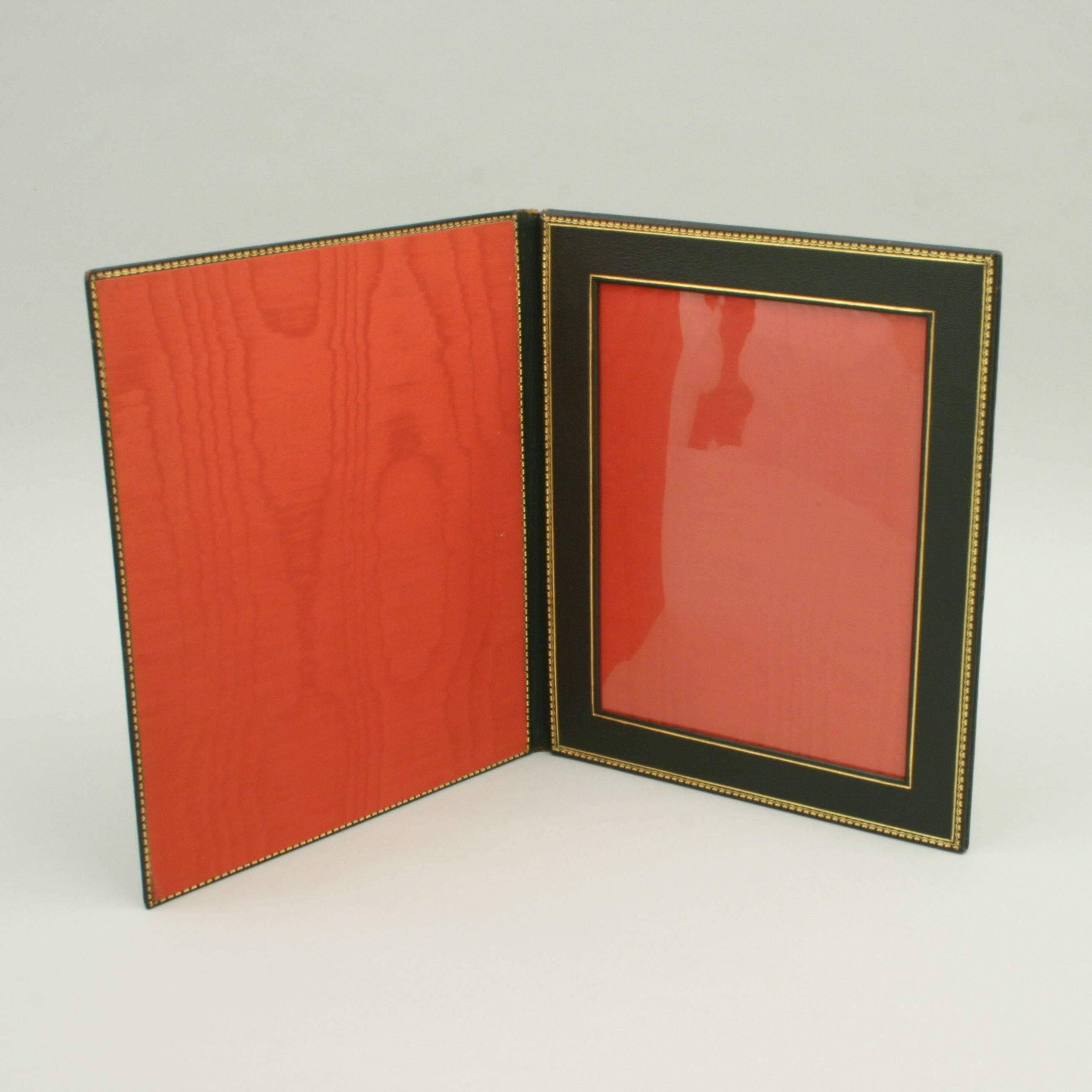 A very nice leather folding travelling photo frame. The outer covering is black leather with fine tooling with initials. The interior with red silk lining and tooled frame. There is a plastic glass to protect the photo, 
circa 1920.