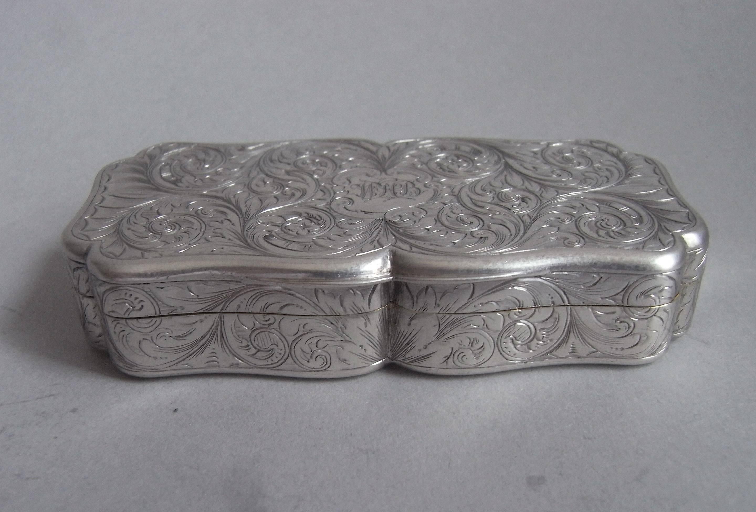 The snuff box is broad rectangular in form with serpentine shaped sides. The exterior is engraved all over with pluming scrolls, foliate designs and a central flower head on the base. The cover displays a Rococo cartouche containing contemporary