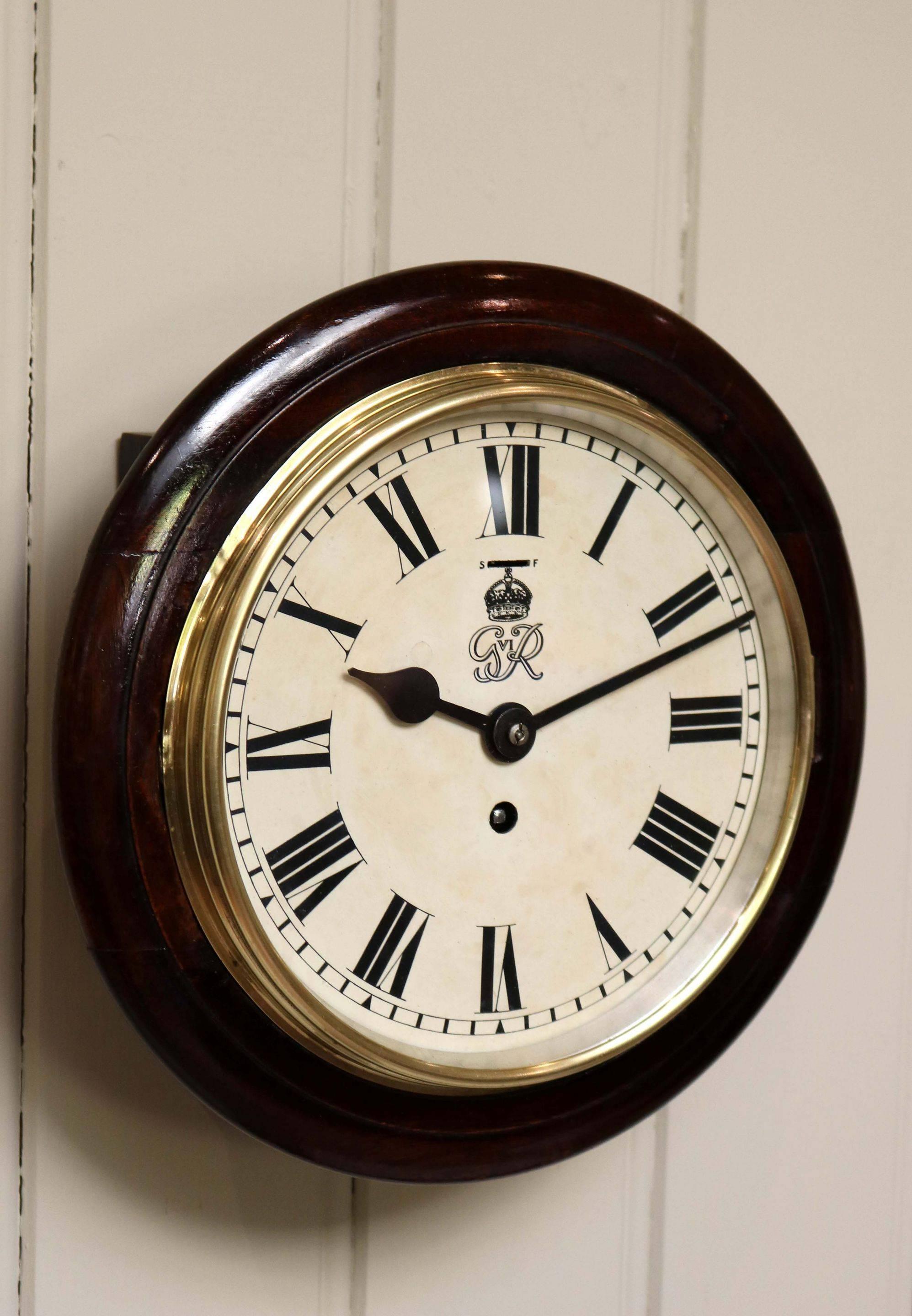 An original solid mahogany cased Post Office/Government Building dial clock, having a turned mahogany rim, with a brass bezel. The white enamel dial has the crest for George VI. The 8 day movement has an 8 day lever platform movement.