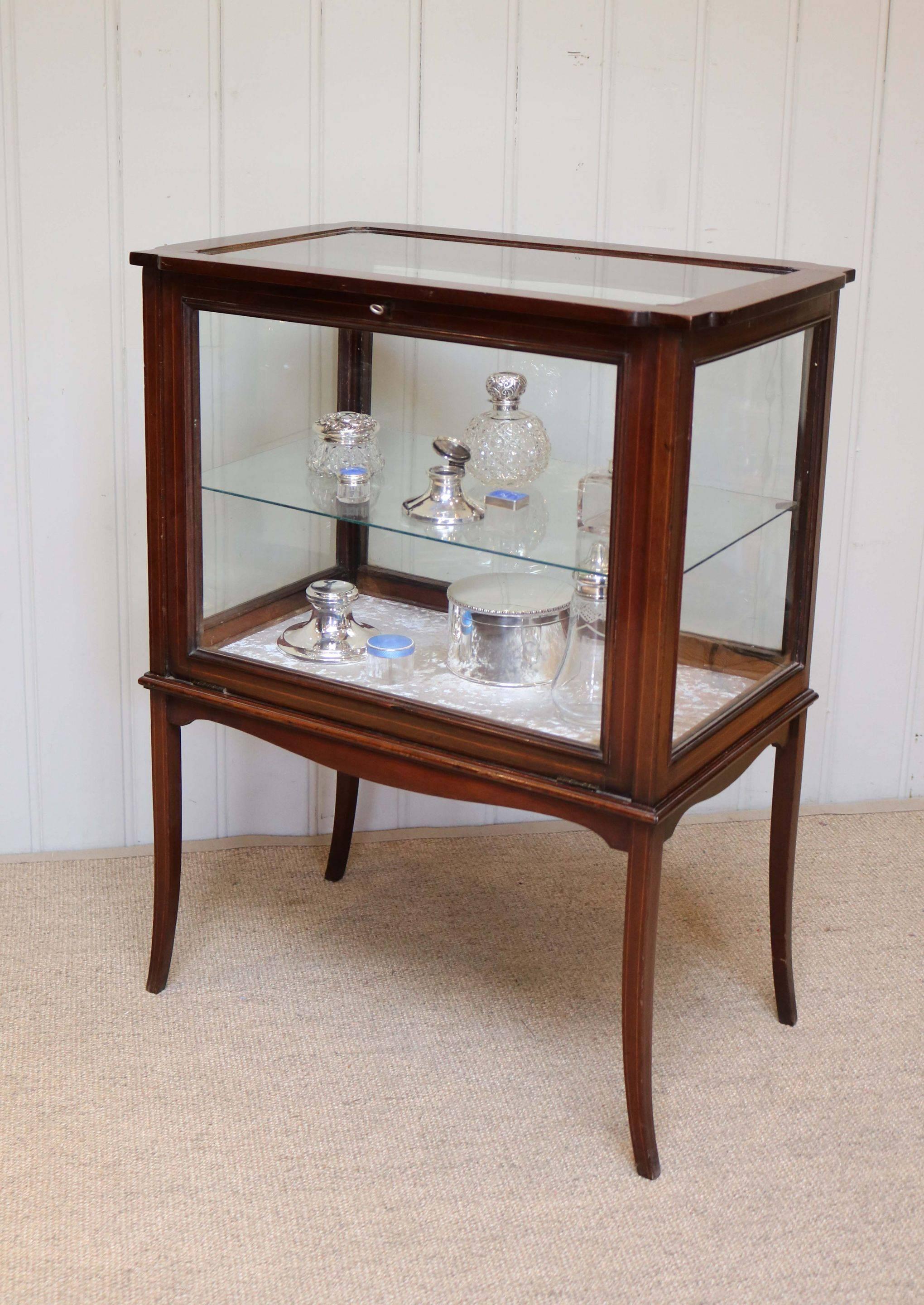 Mahogany bijouterie display cabinet having a shaped top with three glazed sides and a drop down glass door to the front with a velvet lined base below a glass shelf raised on tapering outsplayed legs.