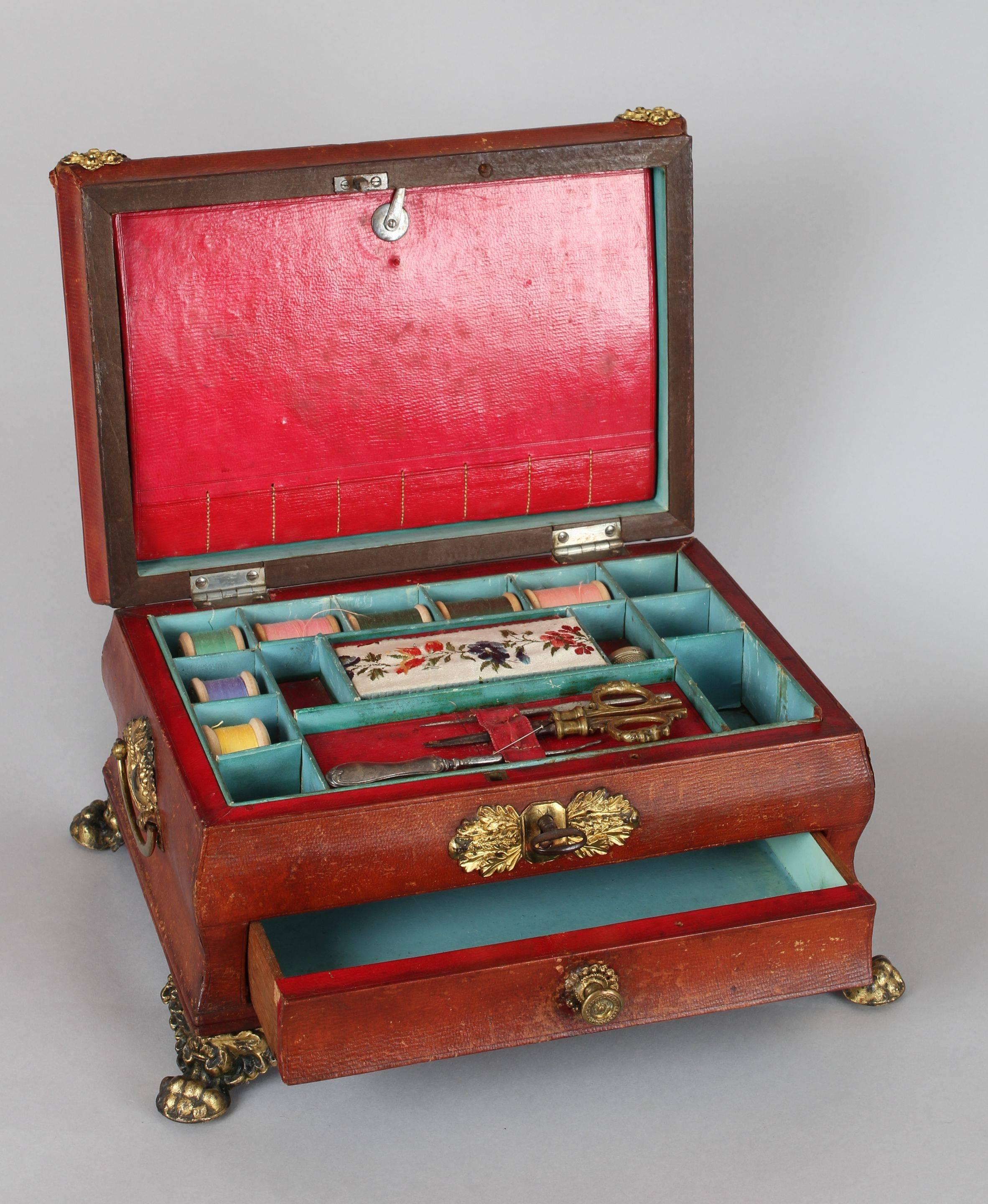 Regency period red Russia-leather work-box of bold bombe shape with a domed and gadrooned lid, flanked by reeded side-pieces and applied with fine cast-brass paw feet, side-handles and decorative mounts; the interior with its original red leather