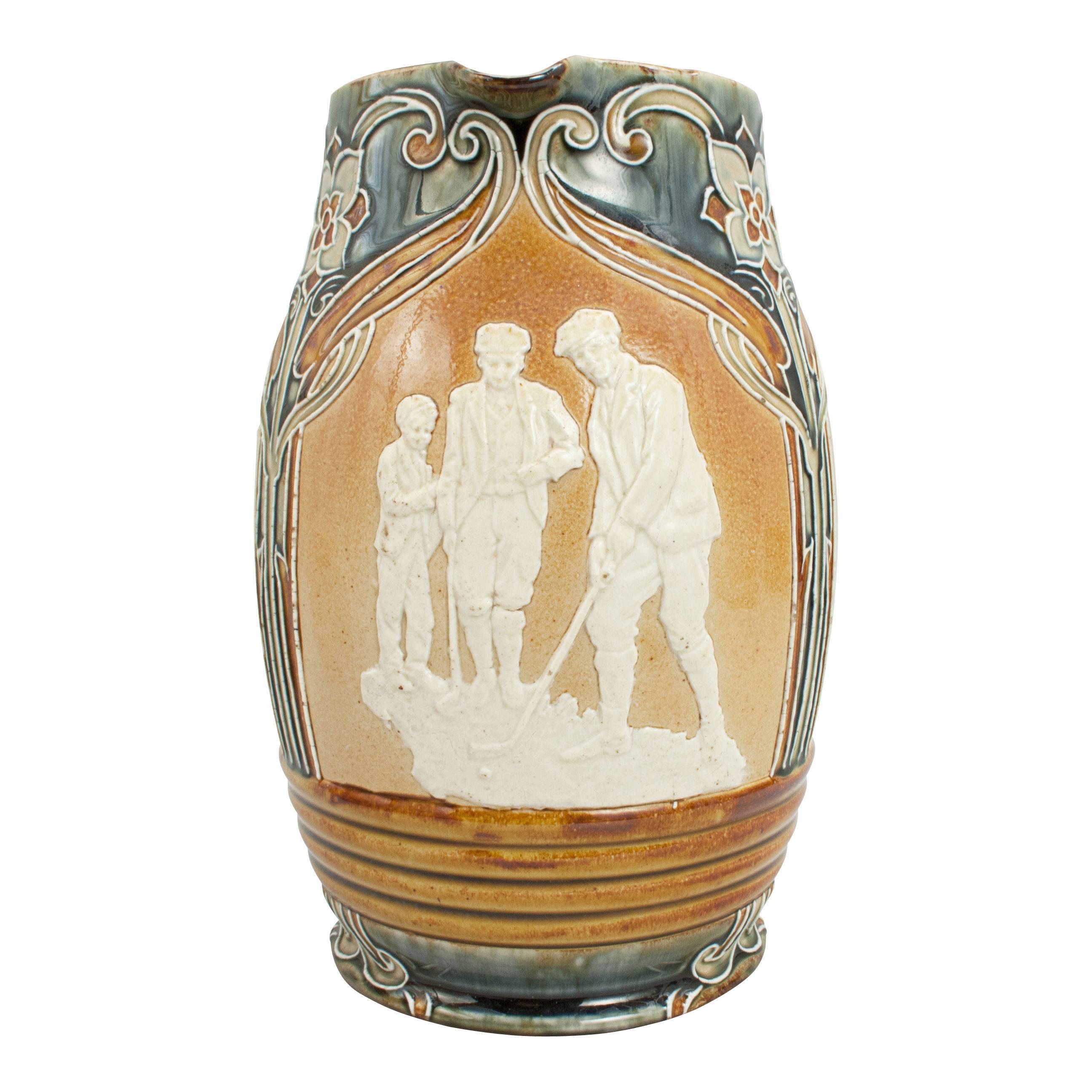 A Royal Doulton Lambeth stoneware jug with Art Nouveau design and golfing scenes in white relief. The designs are based on models by John Broad and are 'Lost Ball, Putting and The Drive'. The base of the jug is stamped 'Doulton Lambeth England' the