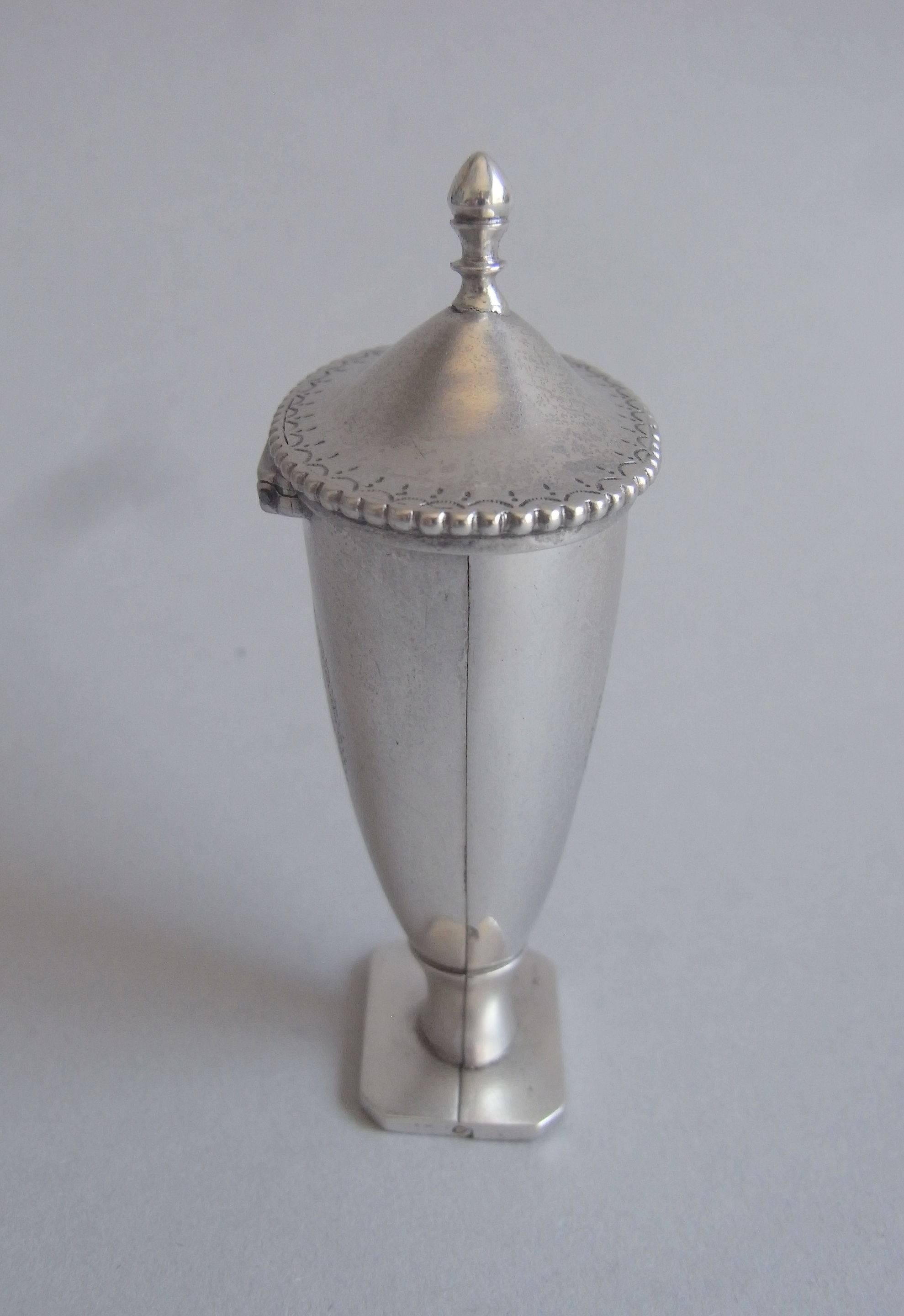 The Nutmeg Grater is beautifully modelled in the very rare vase or urn form and stands on a square foot, with cut corners. The hinged domed cover terminates in a ball finial and displays a beaded bright cut border. Both the front and reverse of the