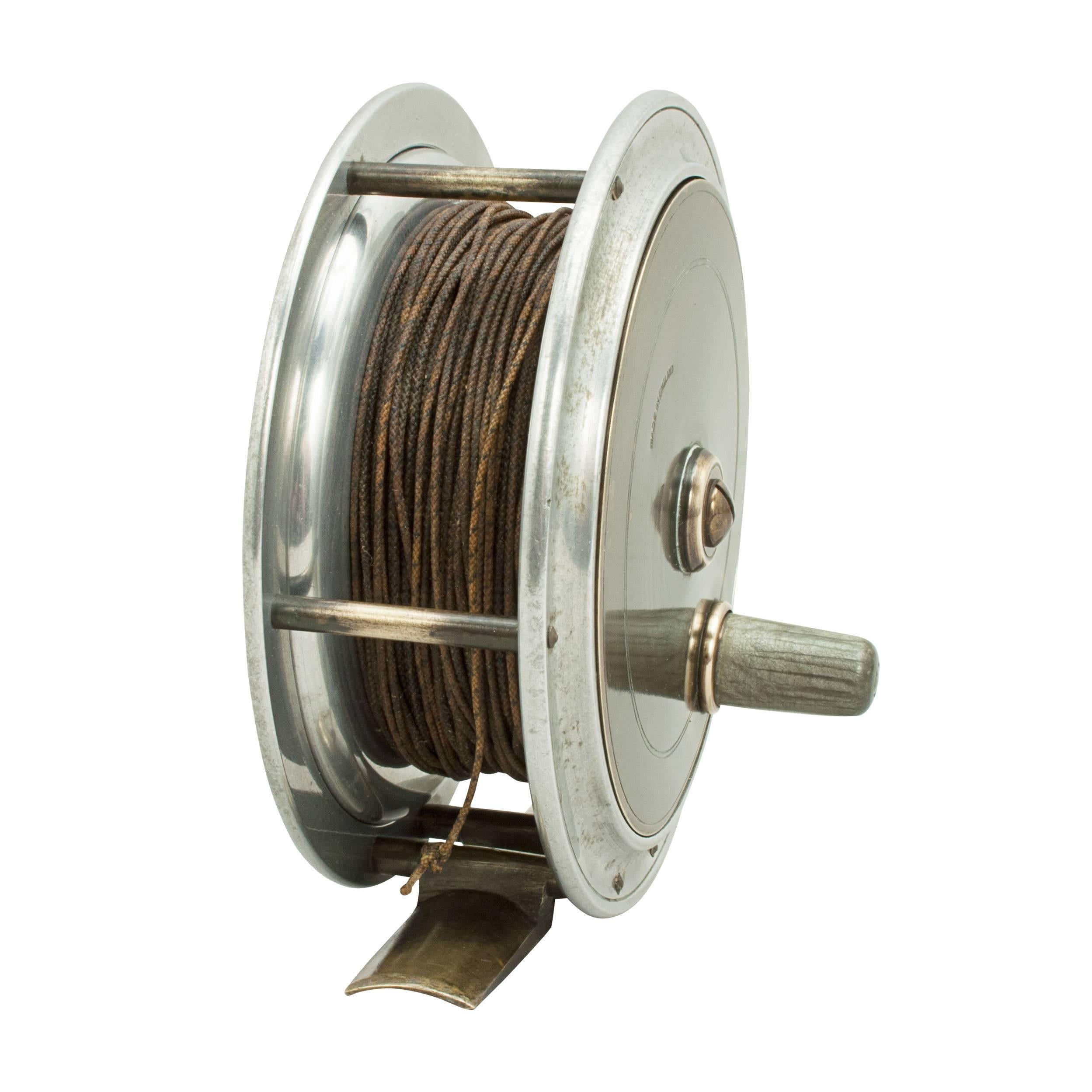 A good alloy Salmon fly fishing reel with brass face, stamped 'Made in England'. The reel with brass foot, optional check and stained wooden winding handle.