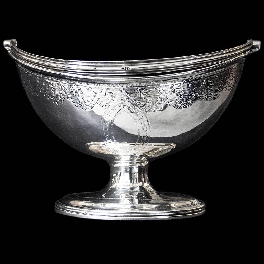 A Georgian silver swing handled sugar basket of oval form on oval pedestal foot. The body and foot decorated with bright cut engraving.