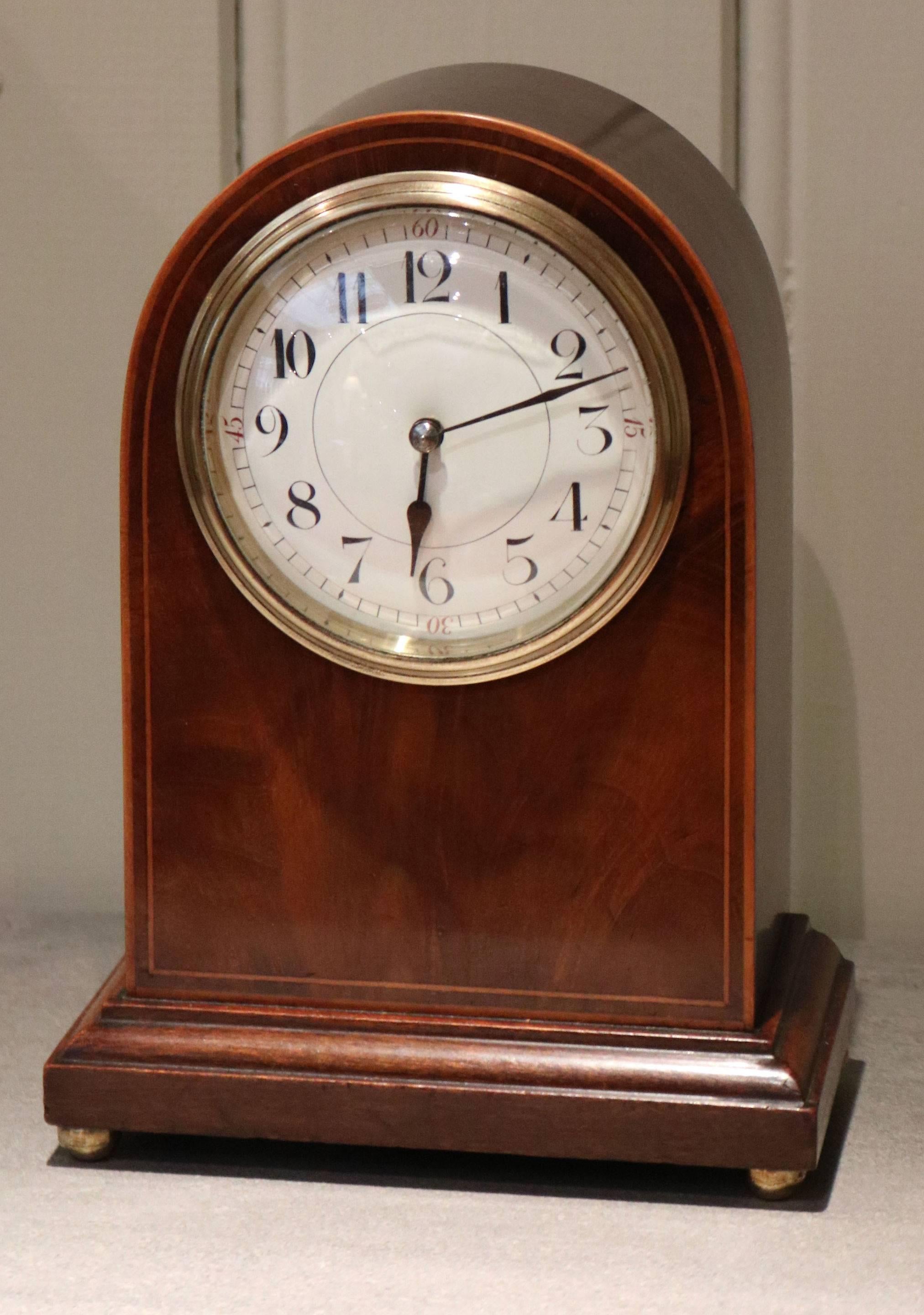 A solid mahogany timepiece mantel clock dating to the early 20th century. It has an arched case, with boxwood stringing and a figured front panel. The enamel dial has a convex glass. It has a French made 8 day movement with a lever platform.