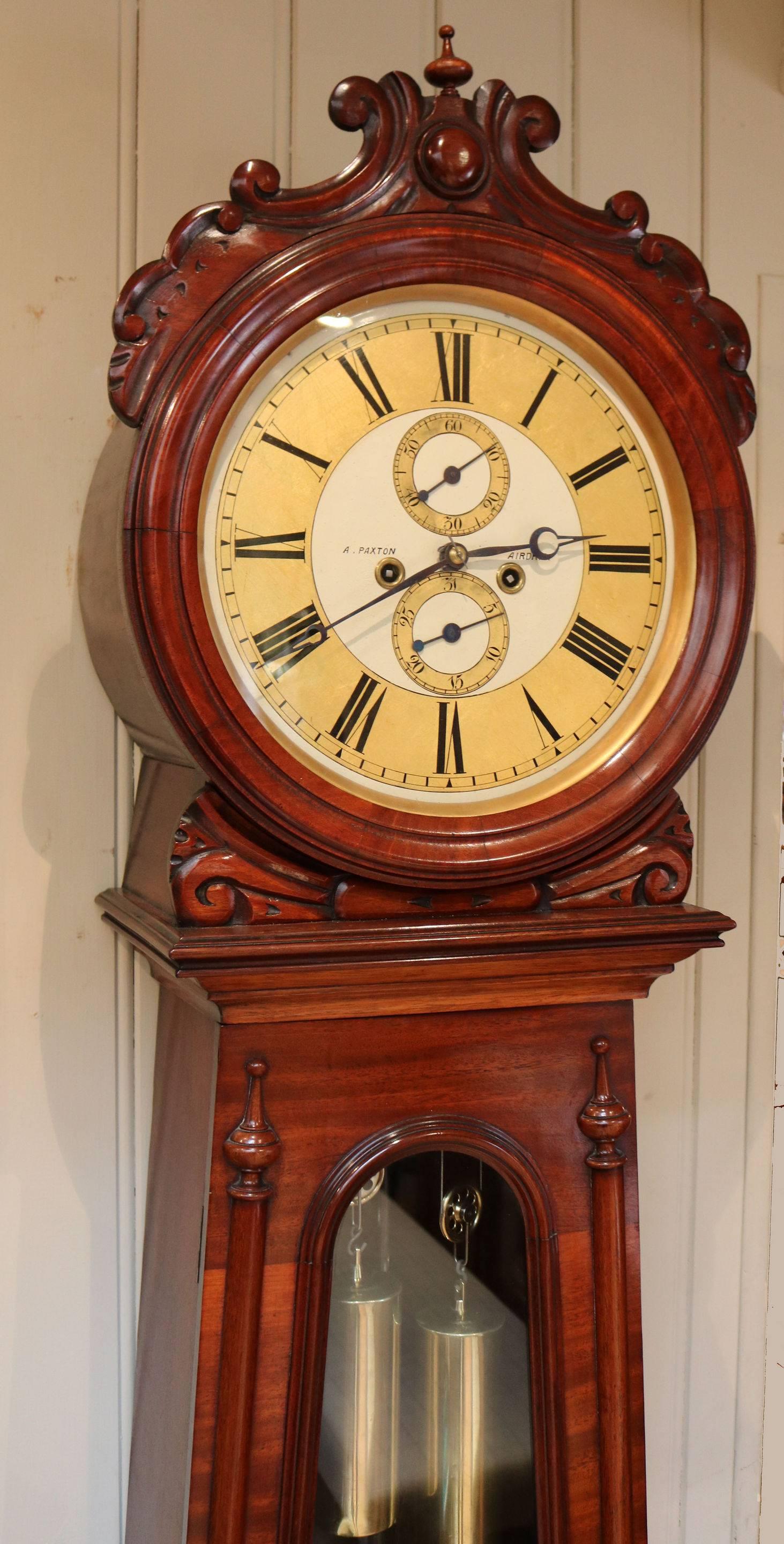 An attractive mid-19th century mahogany longcase clock, of a typical Scottish drumhead form. The case has a circular hood with a carved cresting and a long glazed door and a bombe shaped base. Visible within the door are the brass weights and wood