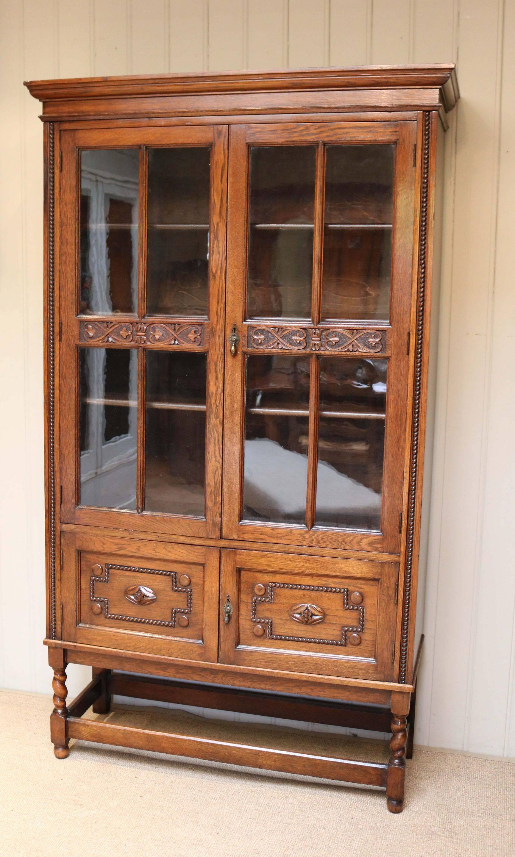 Oak cabinet bookcase having a two-door glazed top section with carved decoration and three internal fully adjustable shelves above a two-door cupboard base raised on short barleytwist legs united by an under stretcher.