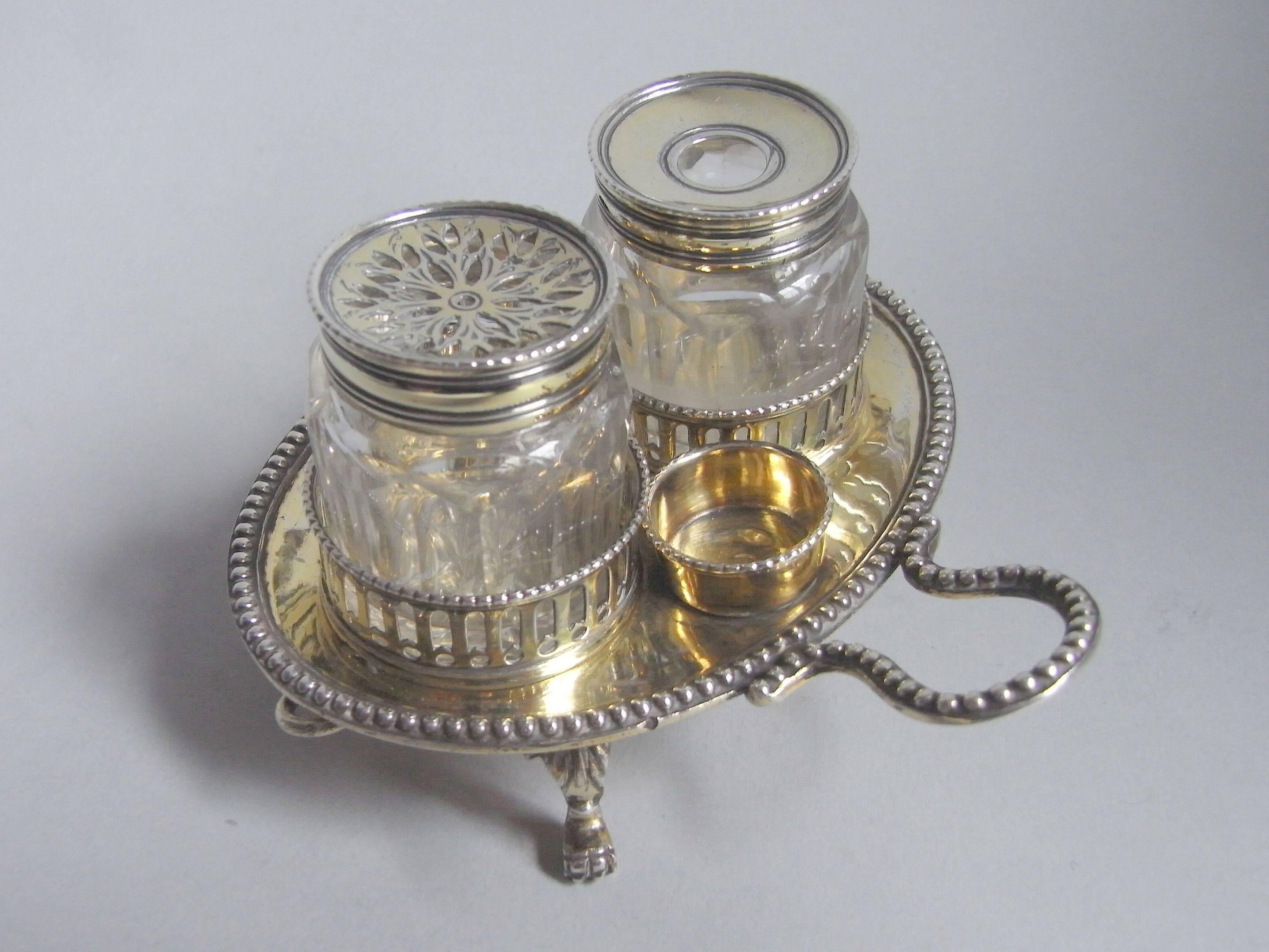 The inkstand has four unusual leaf capped claw and ball feet and an oval stand with beaded edge and carrying handle. The two circular cages are decorated with pierced vertical pails and beading. This example also displays two tubular containers for