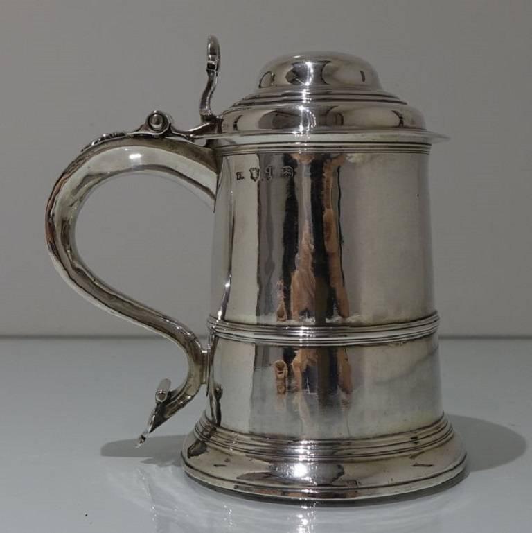 A beautiful tapered cylindrical tankard and cover with domed hinged lid and scroll handle. The tankard has a lower applied wire to the body for highlights and an elegant lower skirt for lowlights. The lid is hinged with a stylish cast thumbpiece and