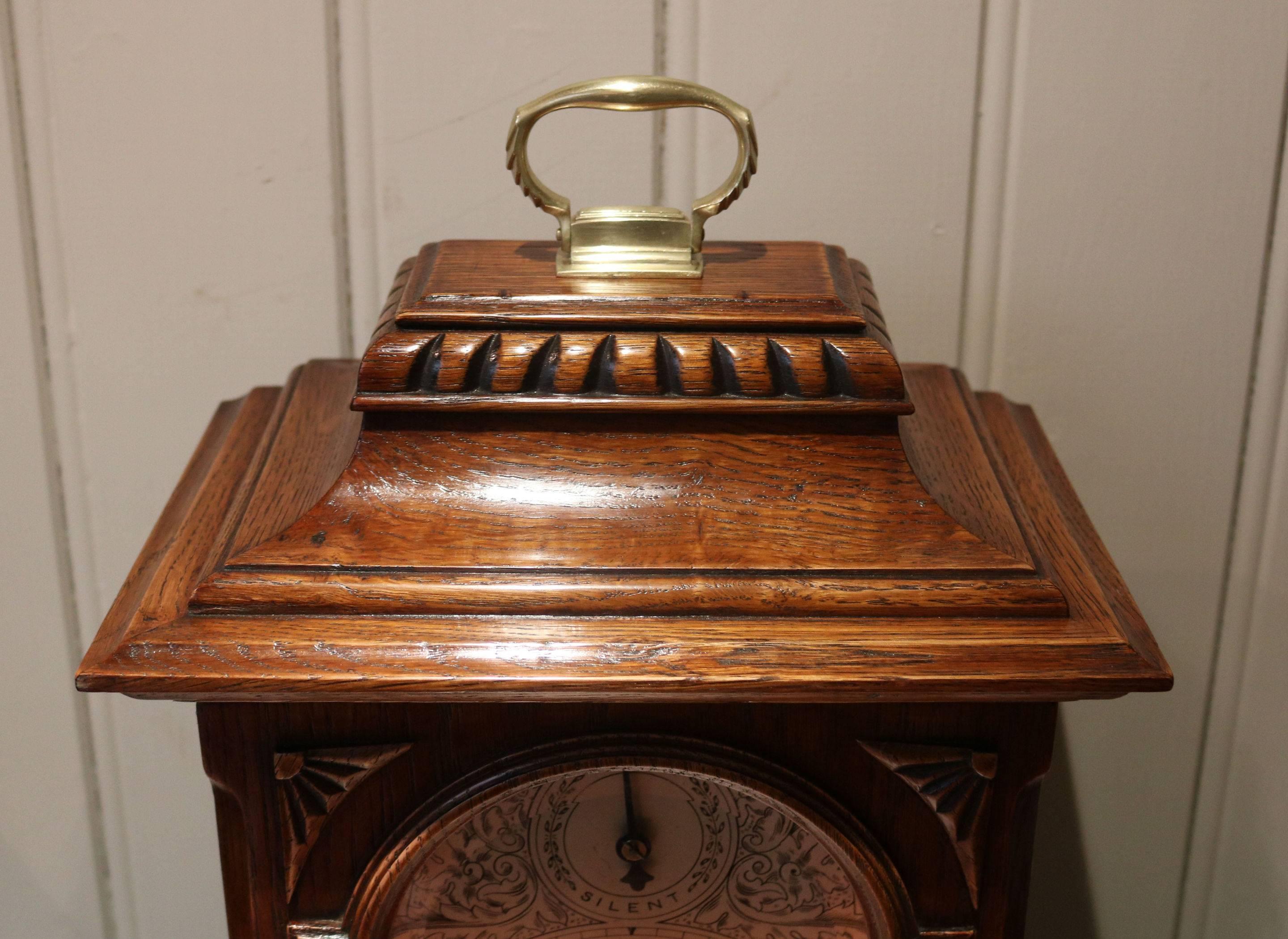 A substantial oak Edwardian Bracket clock, dating to the early 20th Century. It has a bell top with a brass carrying handle, a break arch top door with carved corner fans and bun feet. The silvered dial has a chime/silent feature within the arch.