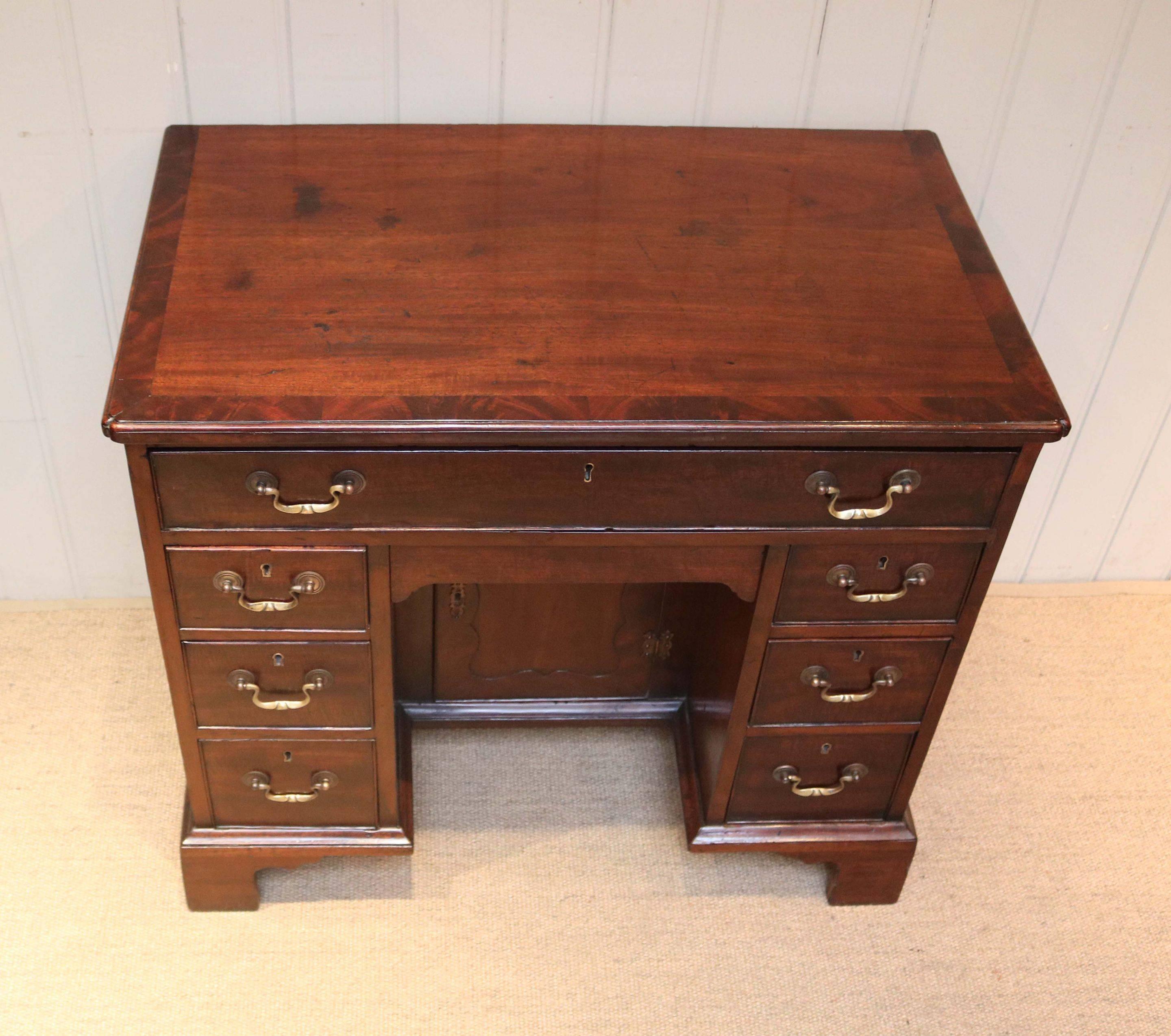 Georgian kneehole desk having a figure crossbanded top with an arrangement of eight oak lined drawers, including a secret frieze drawer, around a central recessed cupboard. Raised on bracket feet.