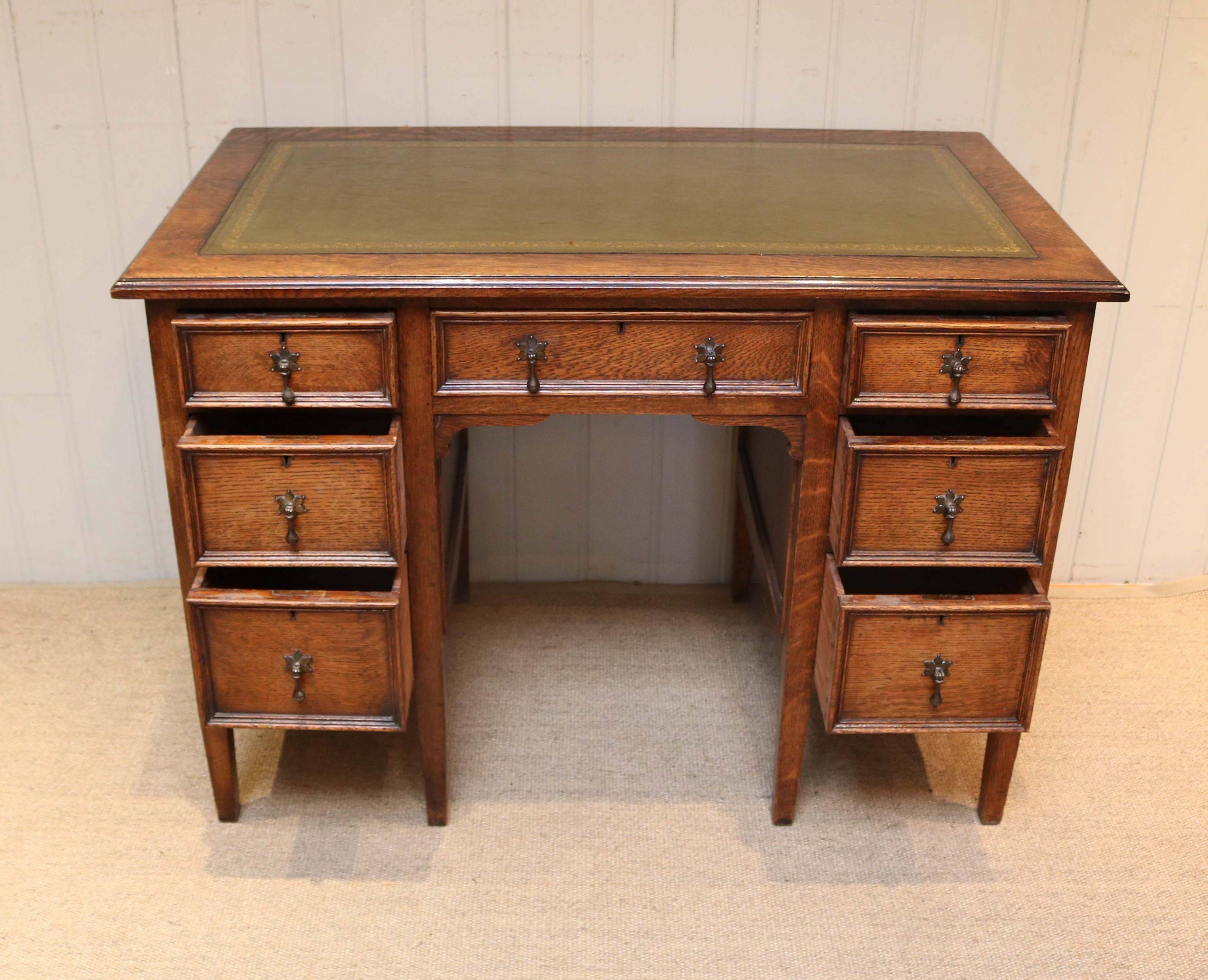 Oak kneehole desk having a central drawer flanked by a further three to either side with panelled sides and a tooled leather top raised on straight tapering legs.
